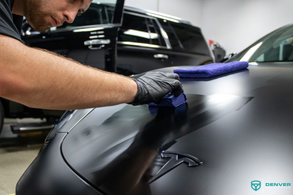 A man is cleaning the hood of a tesla model 3 with a cloth.