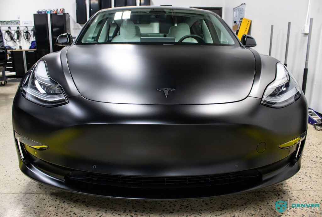 A black tesla model 3 is parked in a garage.