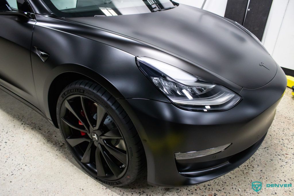 A black tesla model 3 is wrapped in matte black vinyl