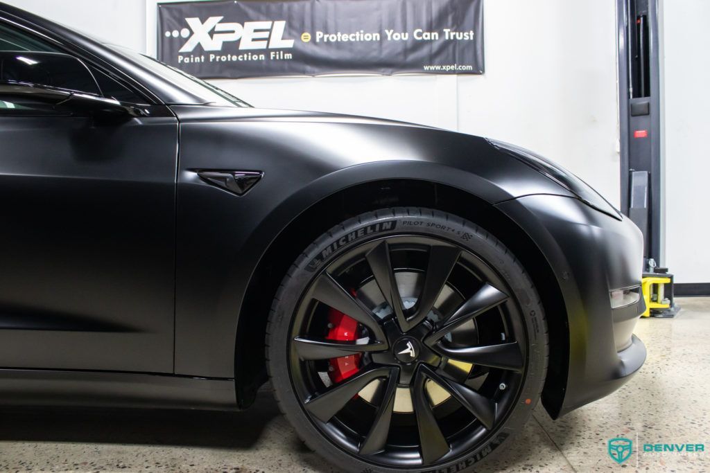 A black tesla model 3 is sitting on a lift in a garage.