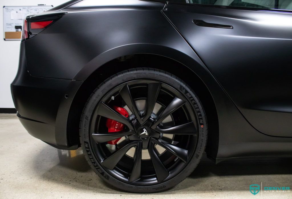 A black tesla model 3 with red brake calipers is parked in a garage.