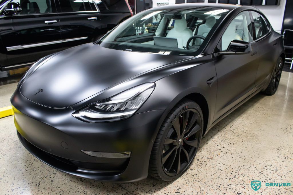 A black tesla model 3 is parked in a garage.