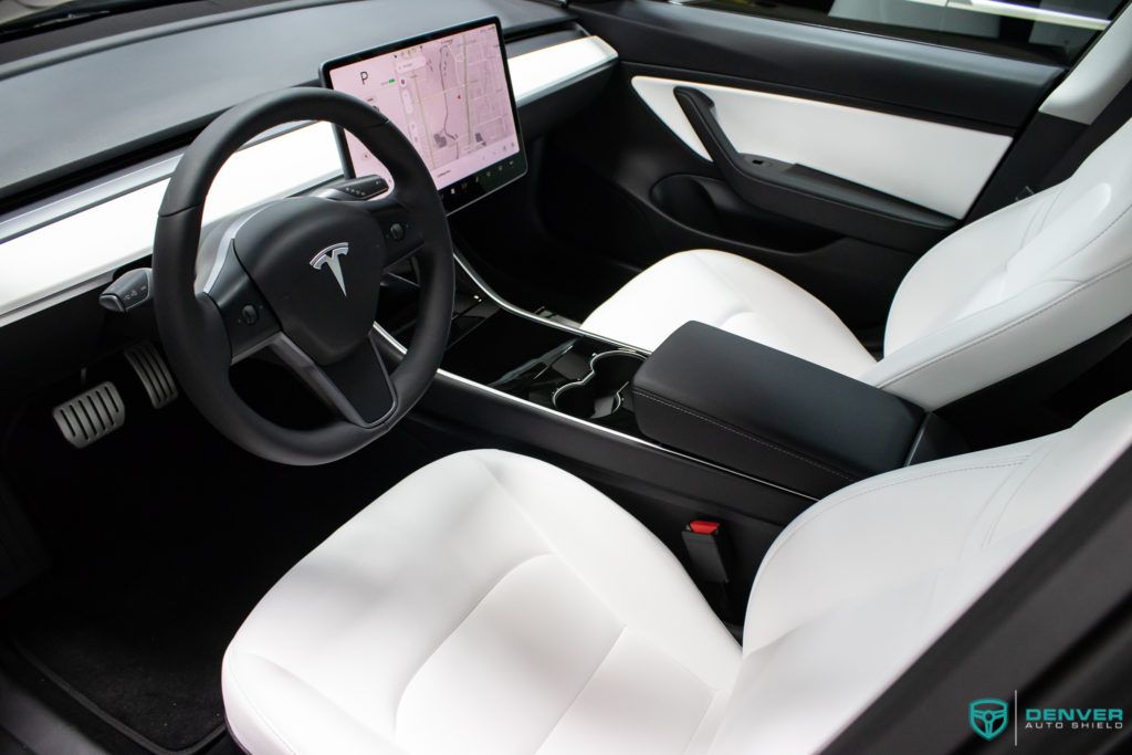 The interior of a tesla model 3 with white seats and a steering wheel.