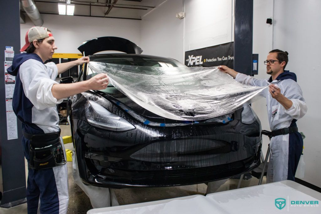 Two men are wrapping a tesla model 3 with a clear film.