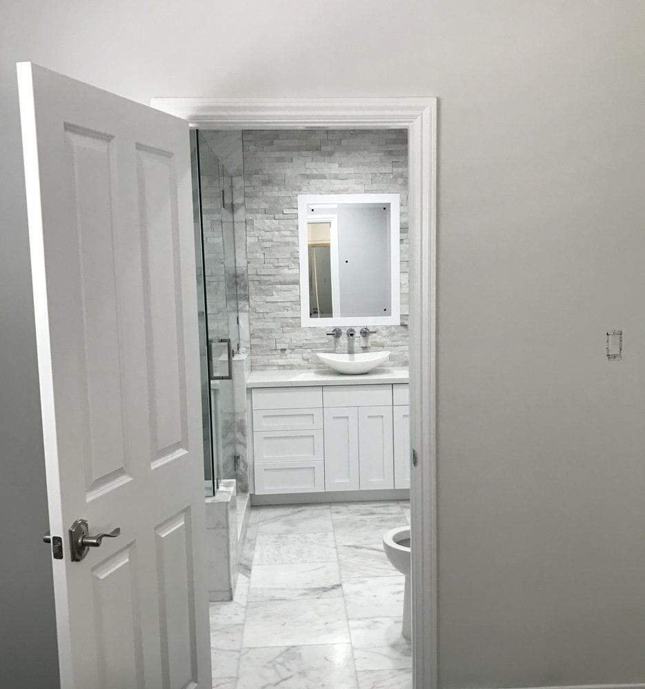 A bathroom with white cabinets , a sink , a toilet and a mirror.