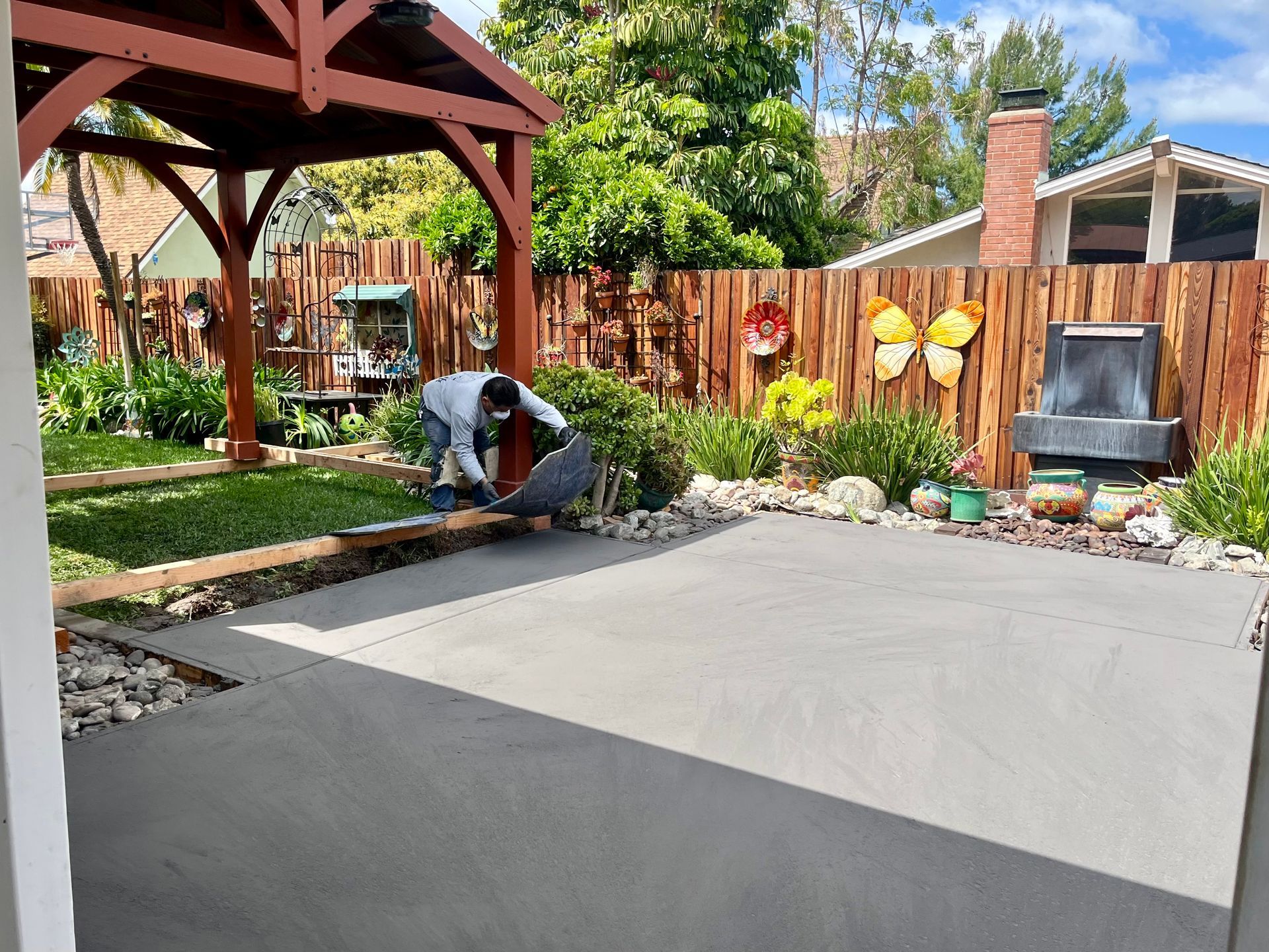 A man is working on a concrete patio in a backyard.