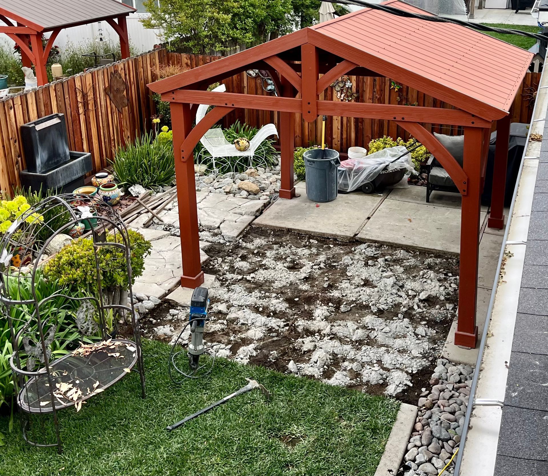A wooden gazebo with a red roof is in the middle of a backyard.