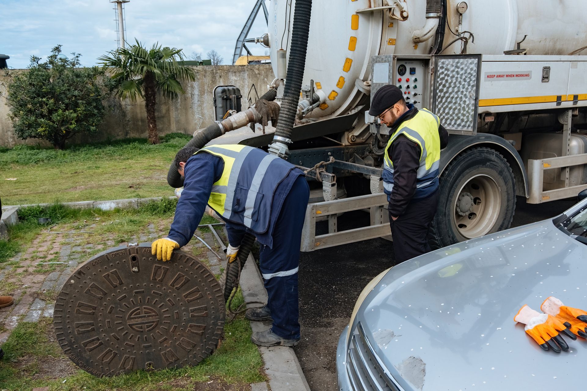 Workers lifting a manhole cover beside a utility truck in a grassy roadside area