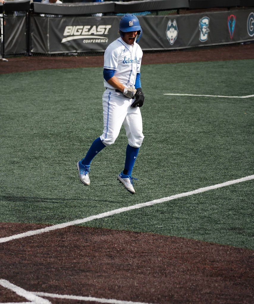 Baseball player in blue-and-white uniform walking on an indoor turf field.