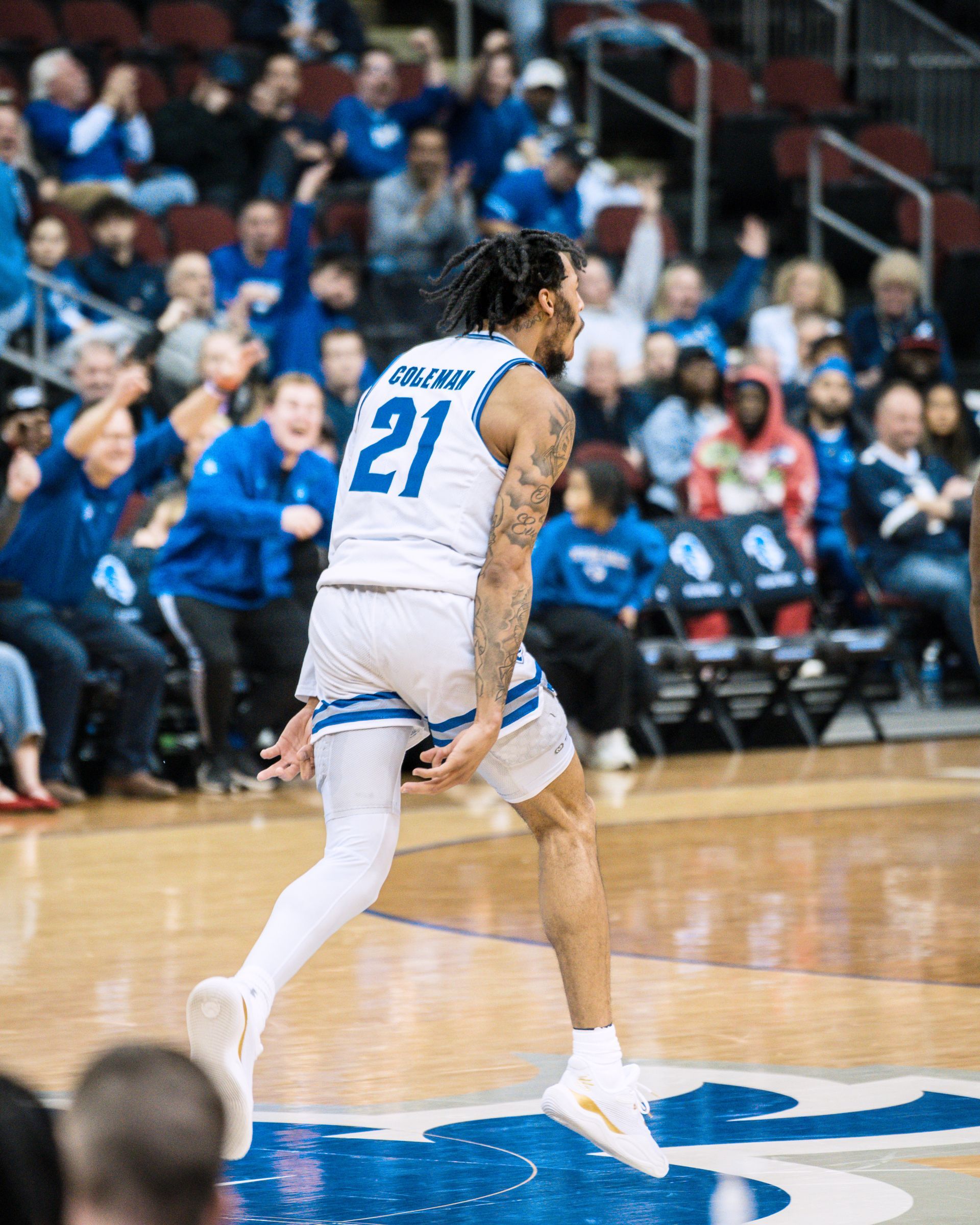 Basketball player in white jersey #21 dribbles on court during a game, crowd seated in the background