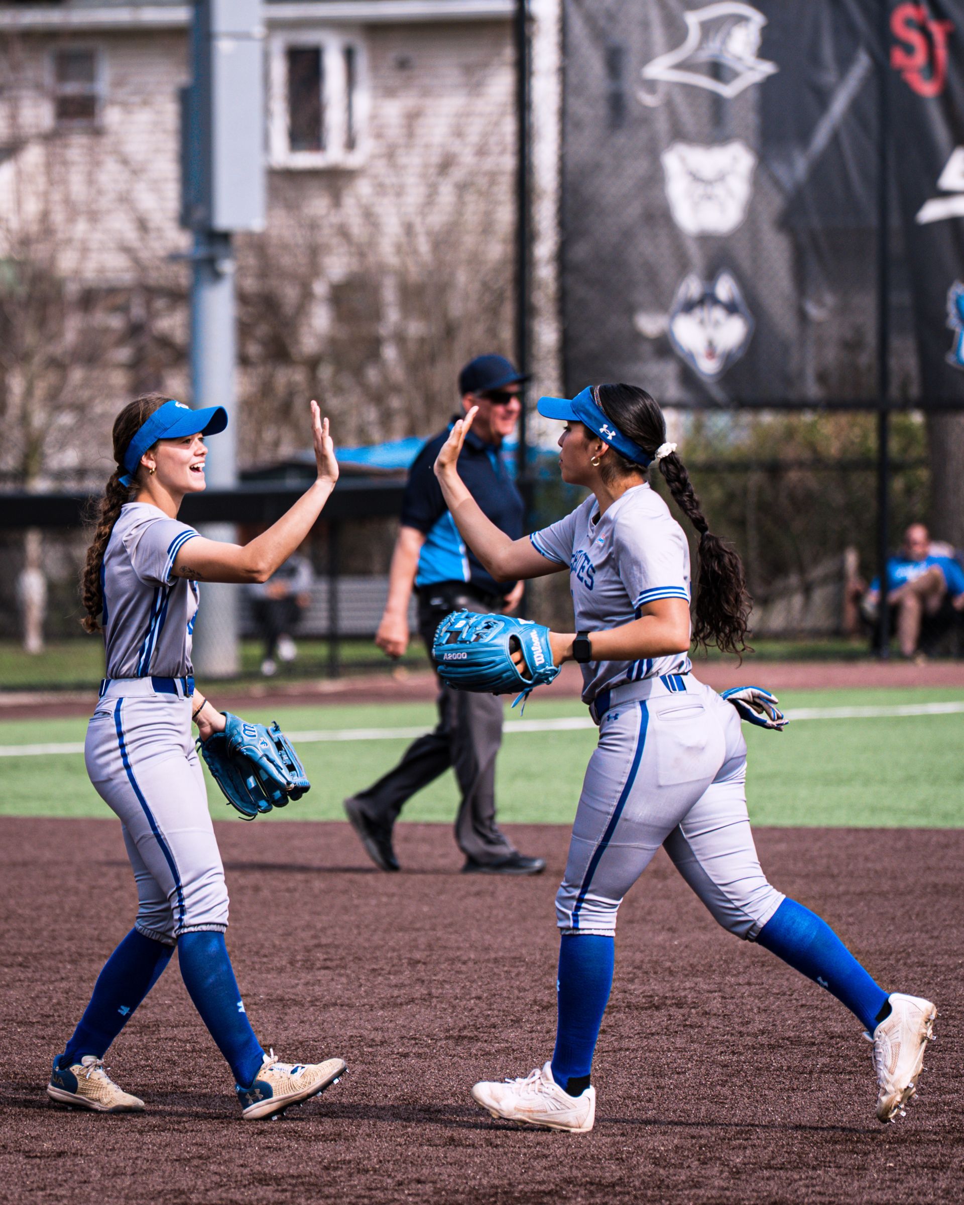 Two softball players in blue uniforms high-five on a field after a play.