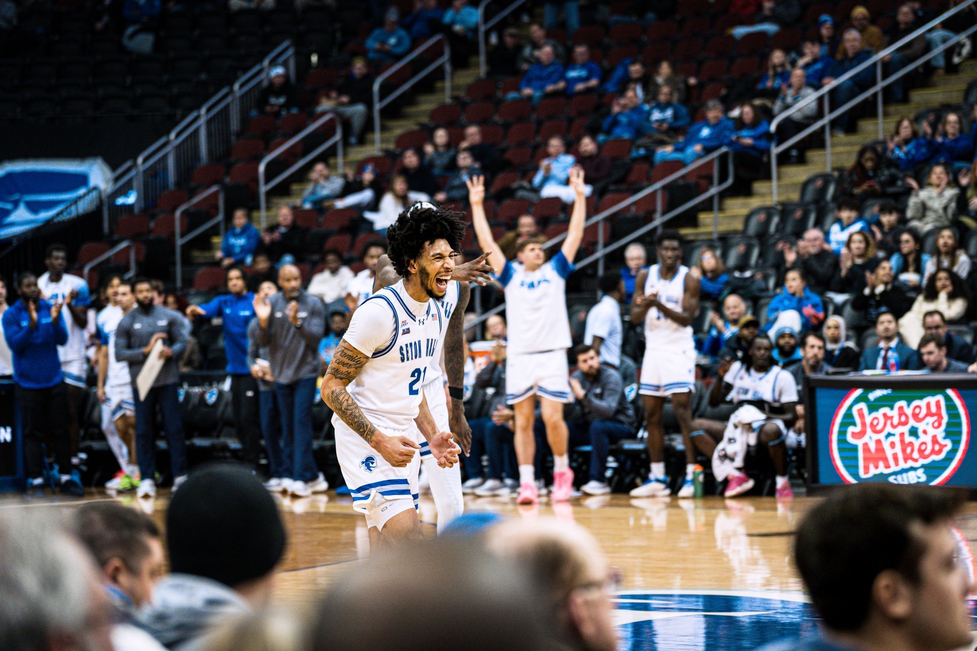 Basketball players in white celebrate on court during a game, with cheering crowd in the stands.