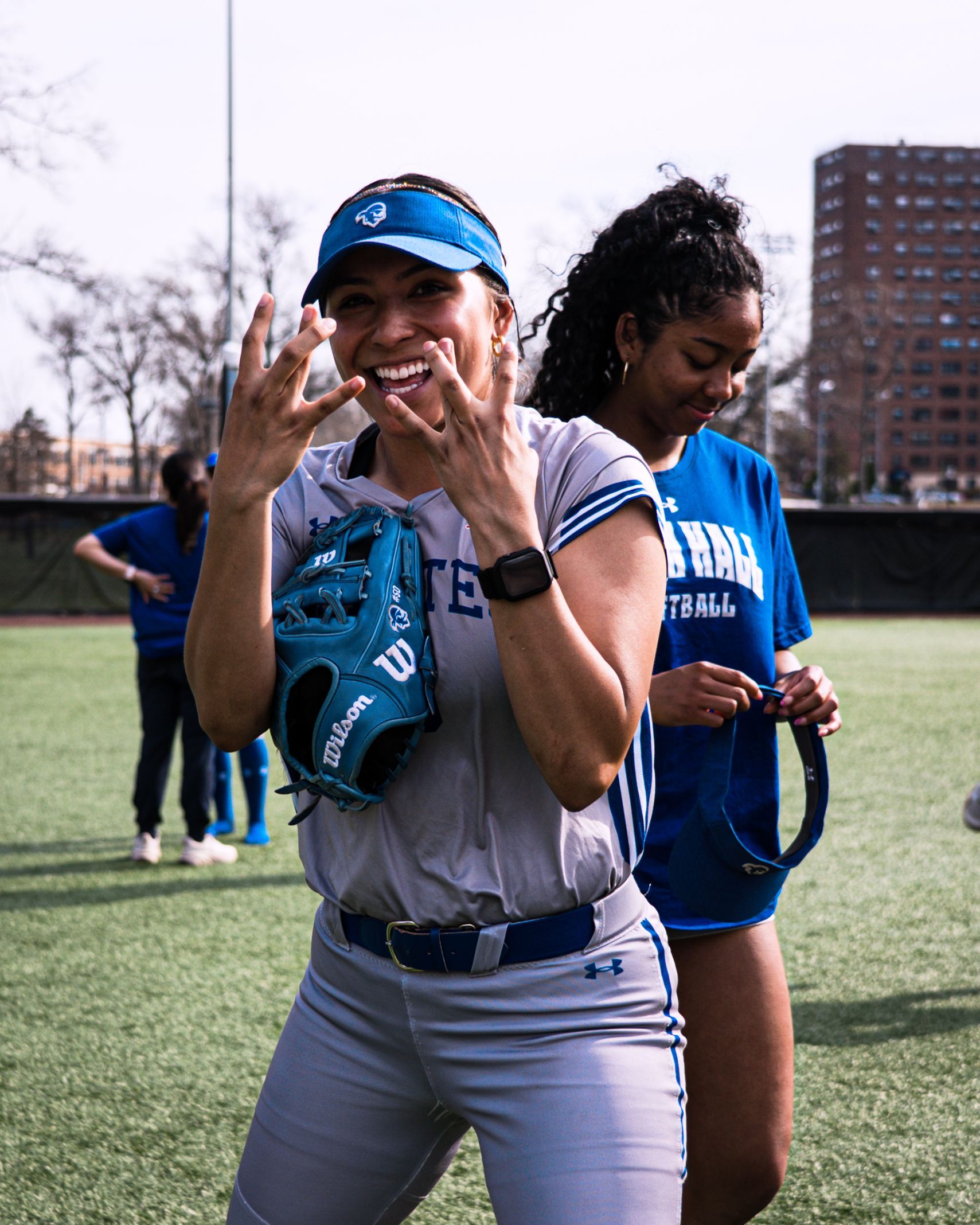 Smiling athlete in blue visor and gray uniform, gesturing on a sports field with another player nearby