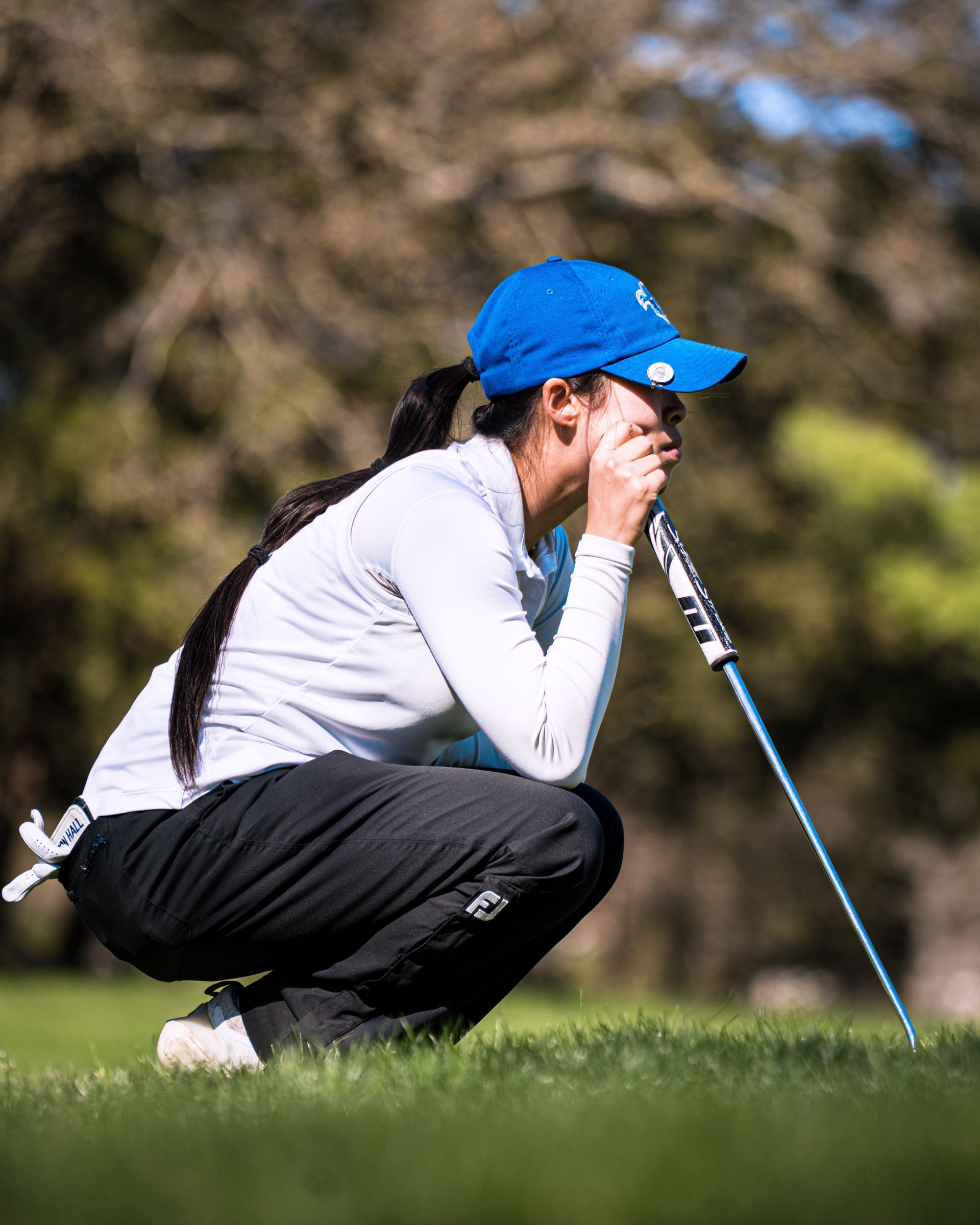 Golfer crouching on the green, lining up a putt with a blue cap and white shirt