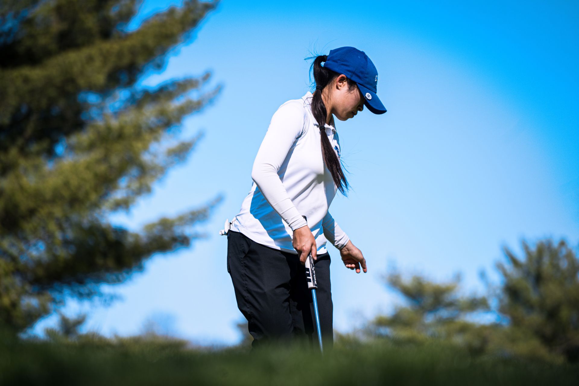 Golfer in blue cap and white top lining up a putt on a green course under a clear sky