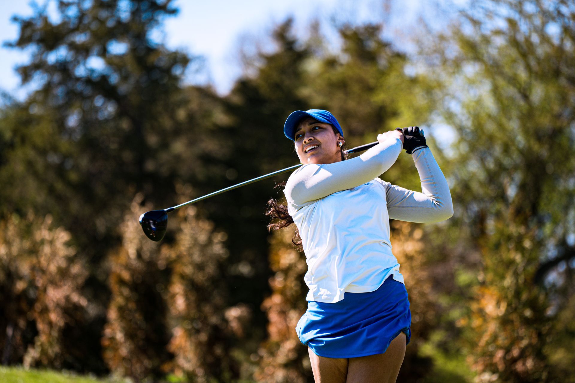 Golfer in white shirt and blue skirt swinging a club on a sunny course