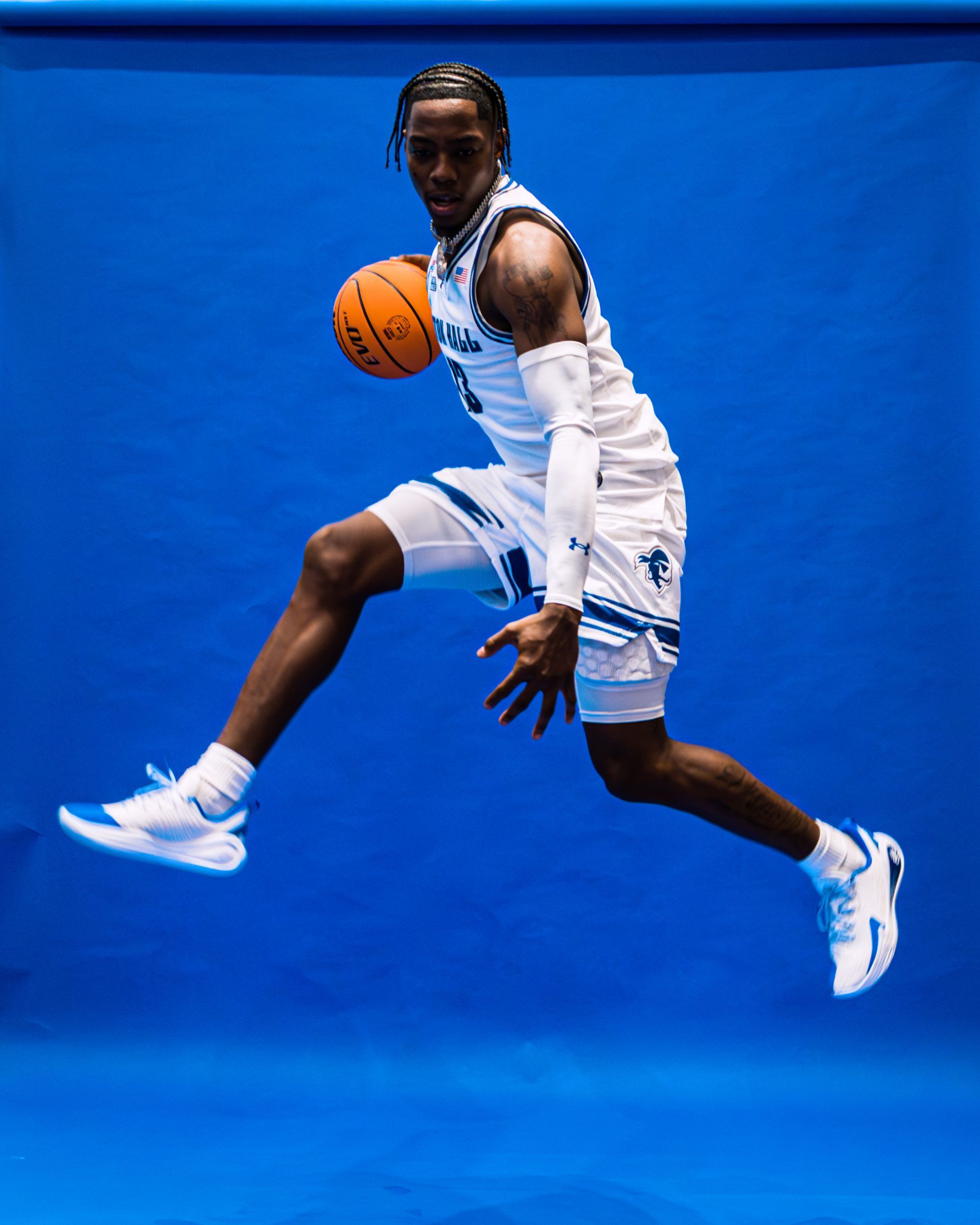 Basketball player in white uniform leaping with ball against a blue background