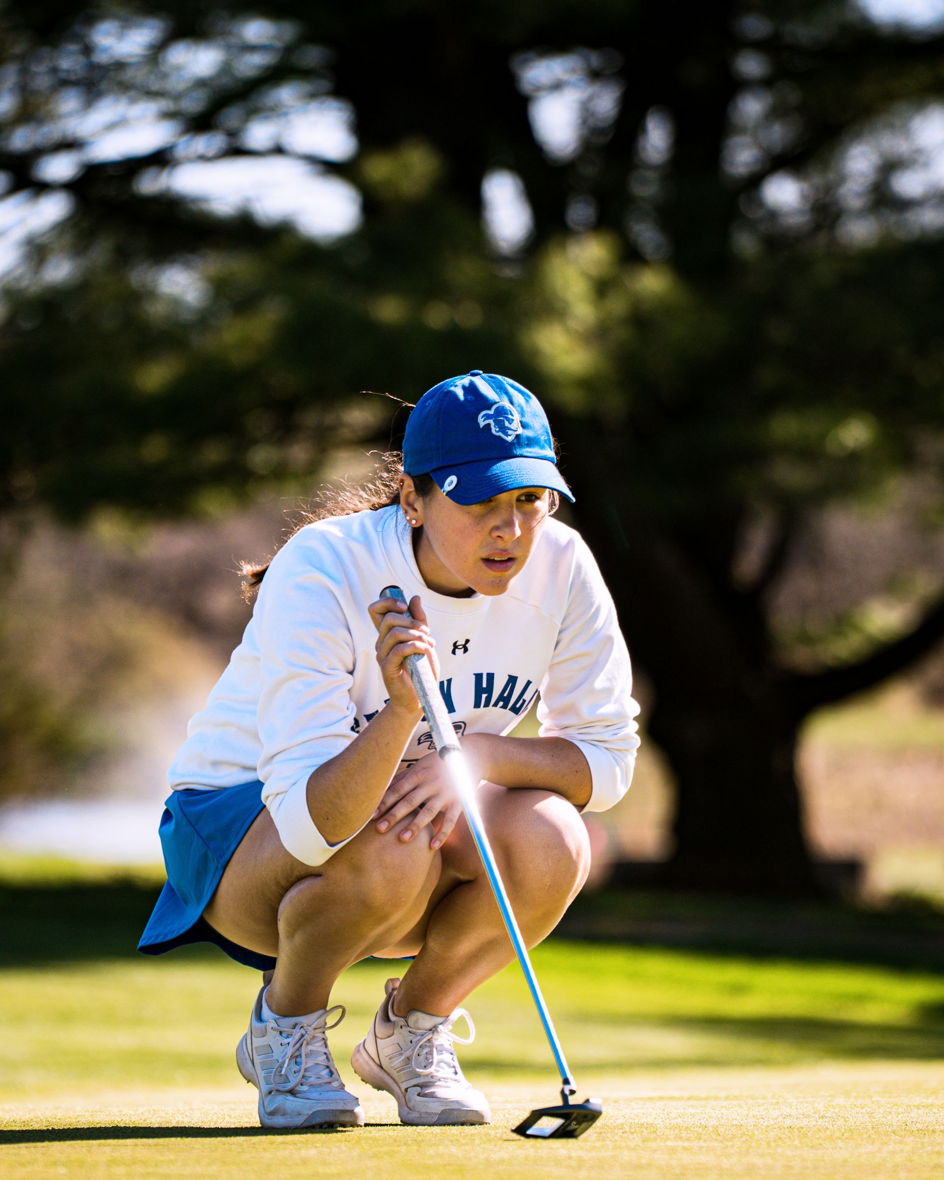 Golfer crouching on the green, lining up a putt with a blue cap and white outfit