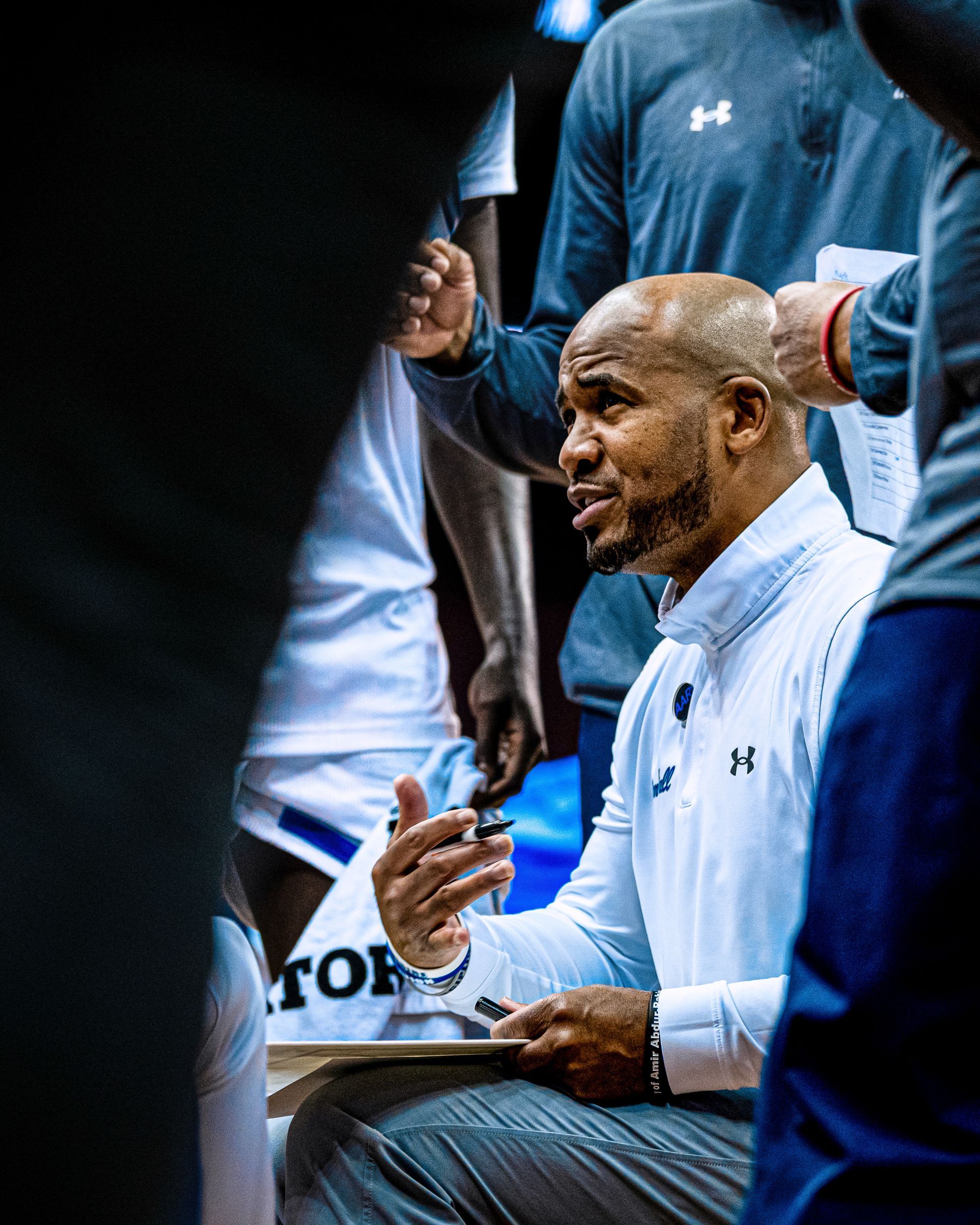 Basketball coach in white jacket gesturing during a timeout on the sideline