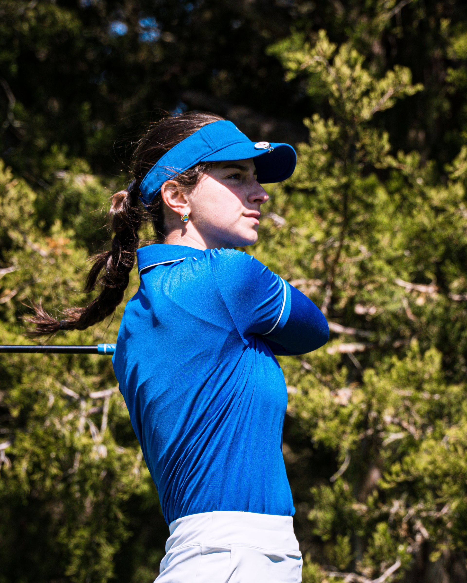 Golfer in blue shirt and visor mid-swing on a sunny course