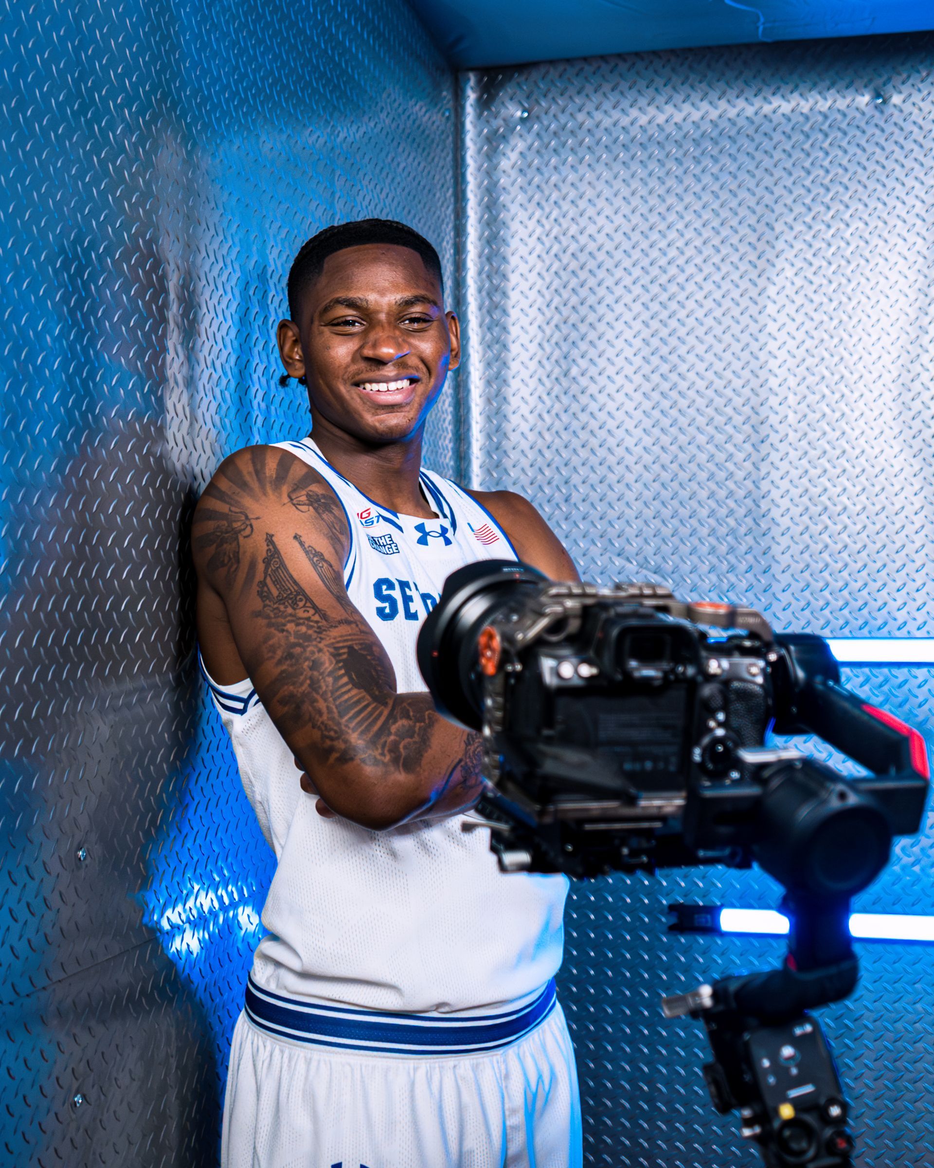 Basketball player in white uniform posing with a camera in a blue studio