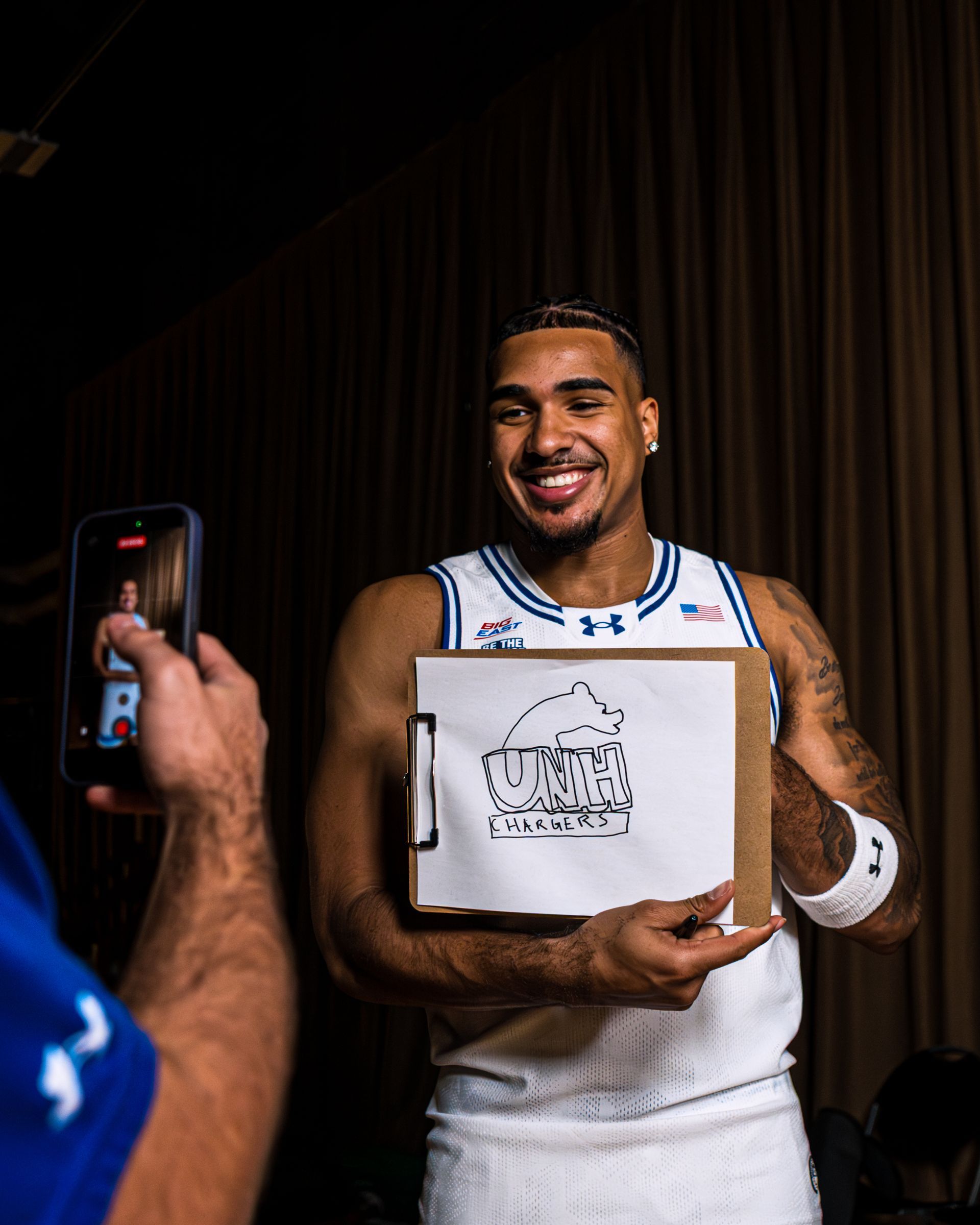 Basketball player in a white jersey smiling and holding an award box while being photographed.