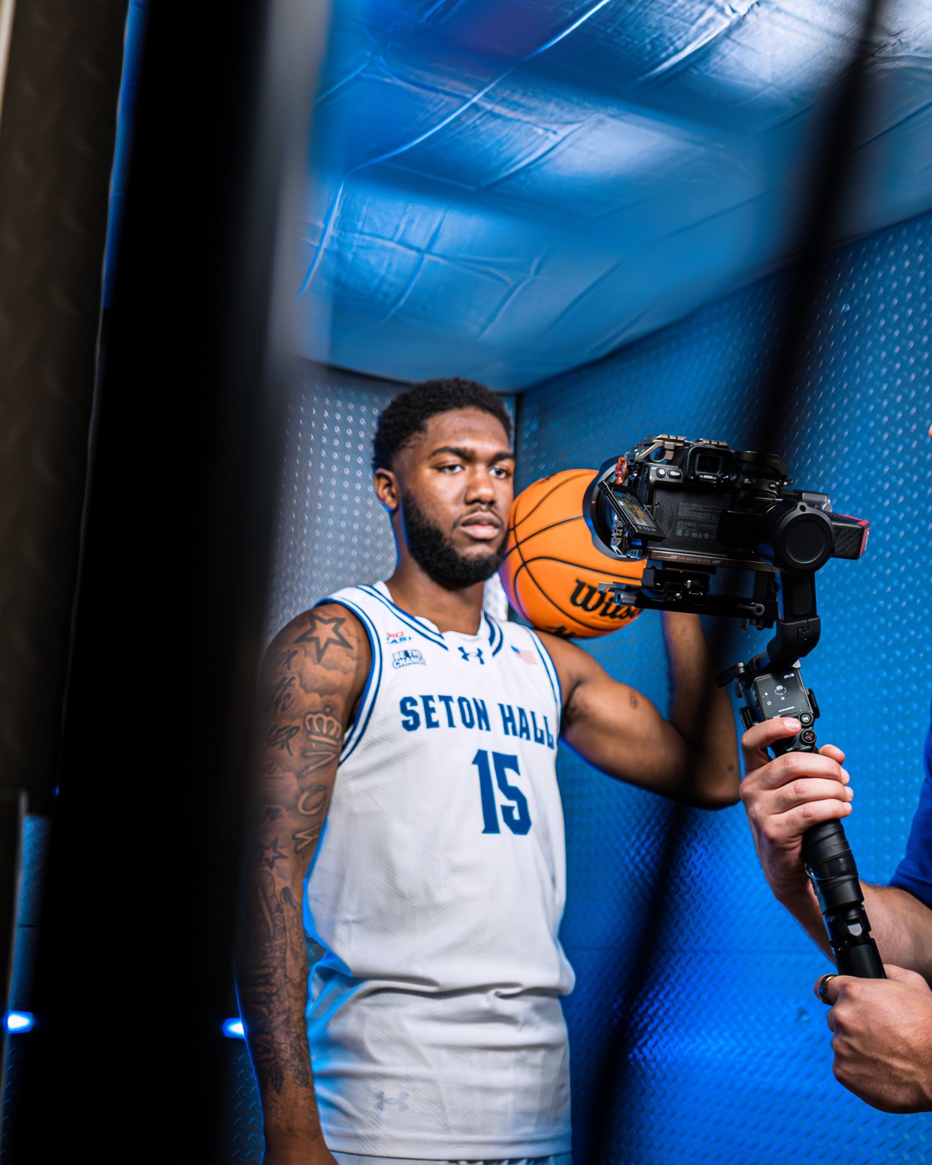 Basketball player in a white jersey posing with a camera in a blue-lit studio