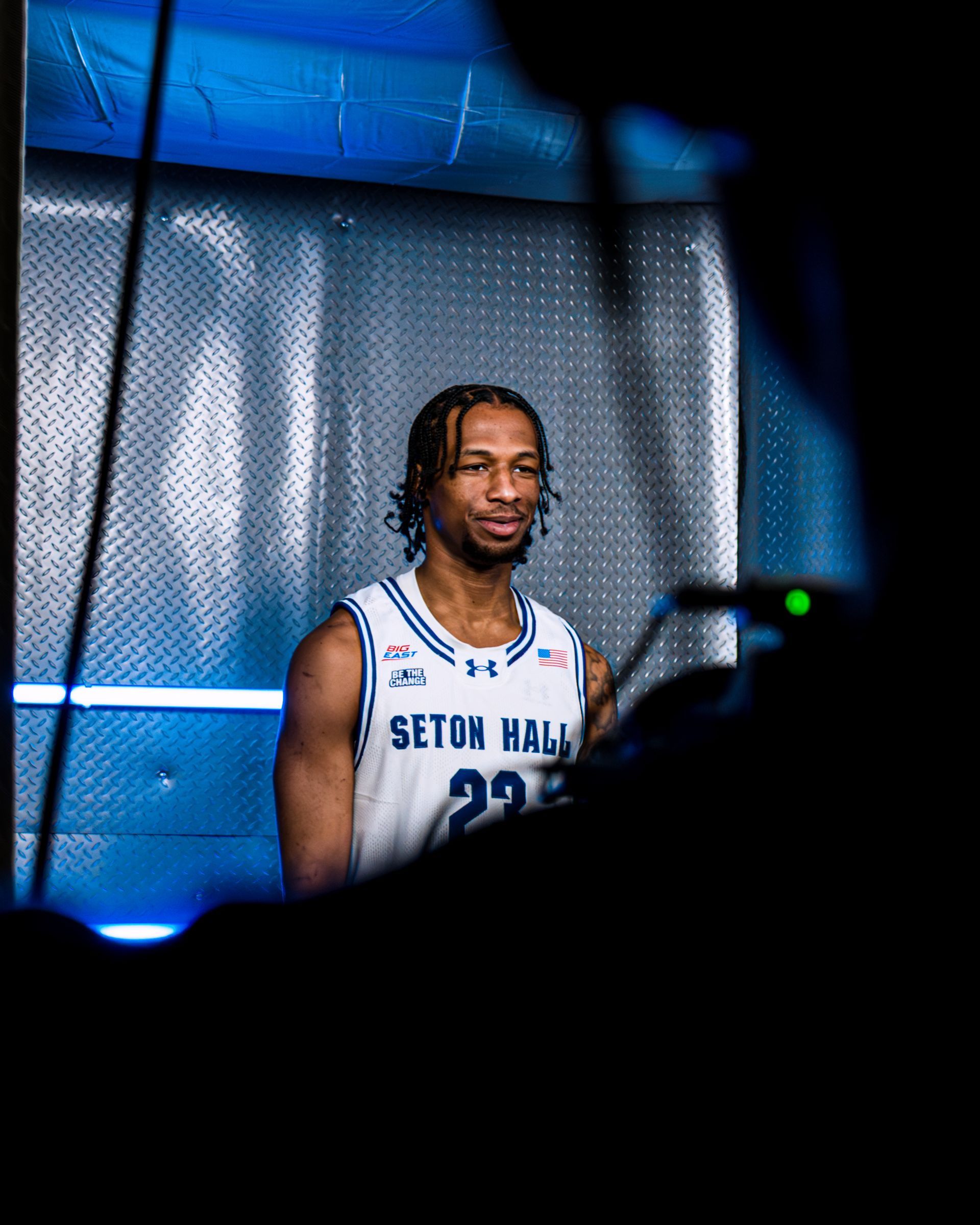 Basketball player in a white Seton Hall jersey posing against a blue studio backdrop
