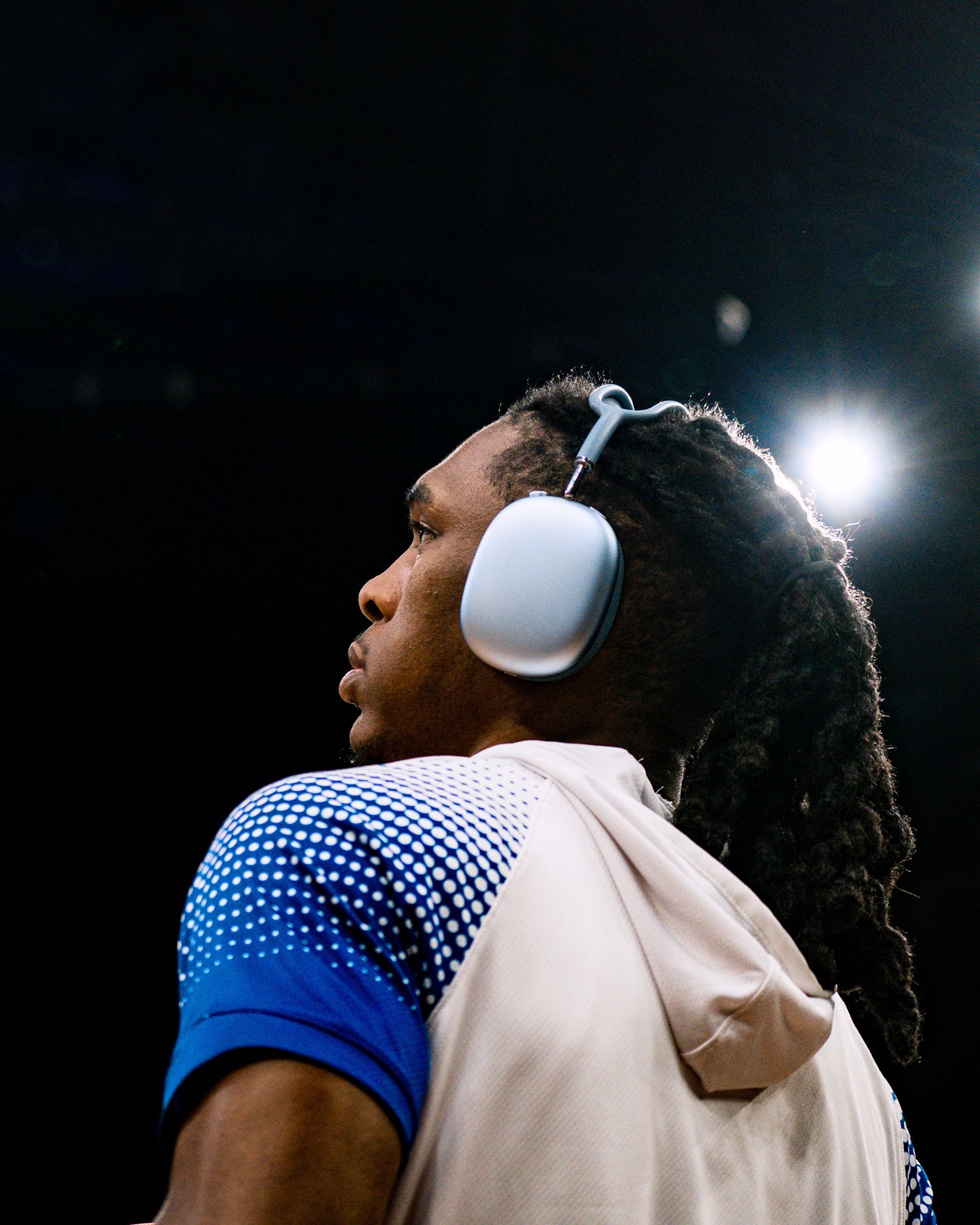 Athlete in white headphones and blue jersey, looking up under stadium lights at night