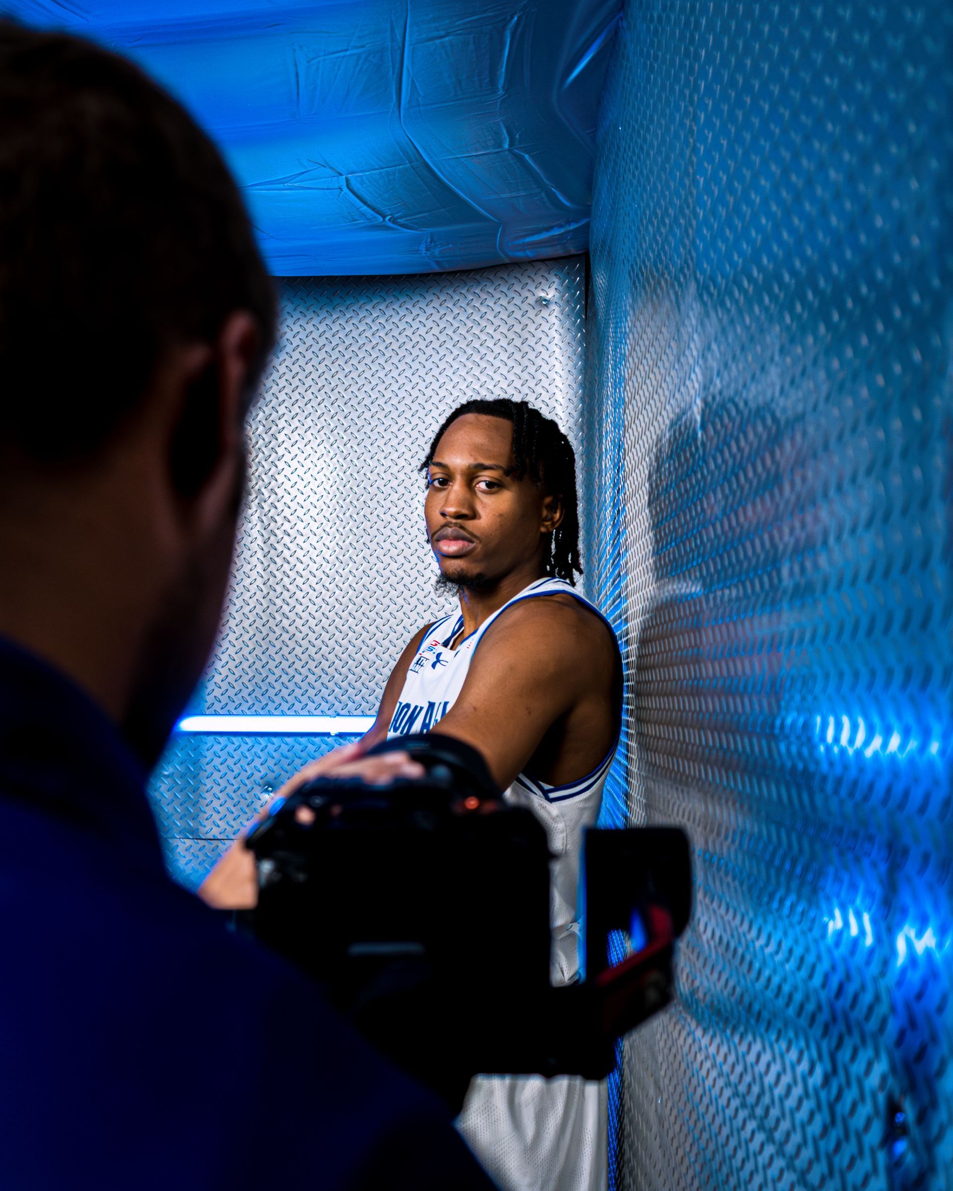 Man posing in blue-lit studio while a camera films him from the foreground