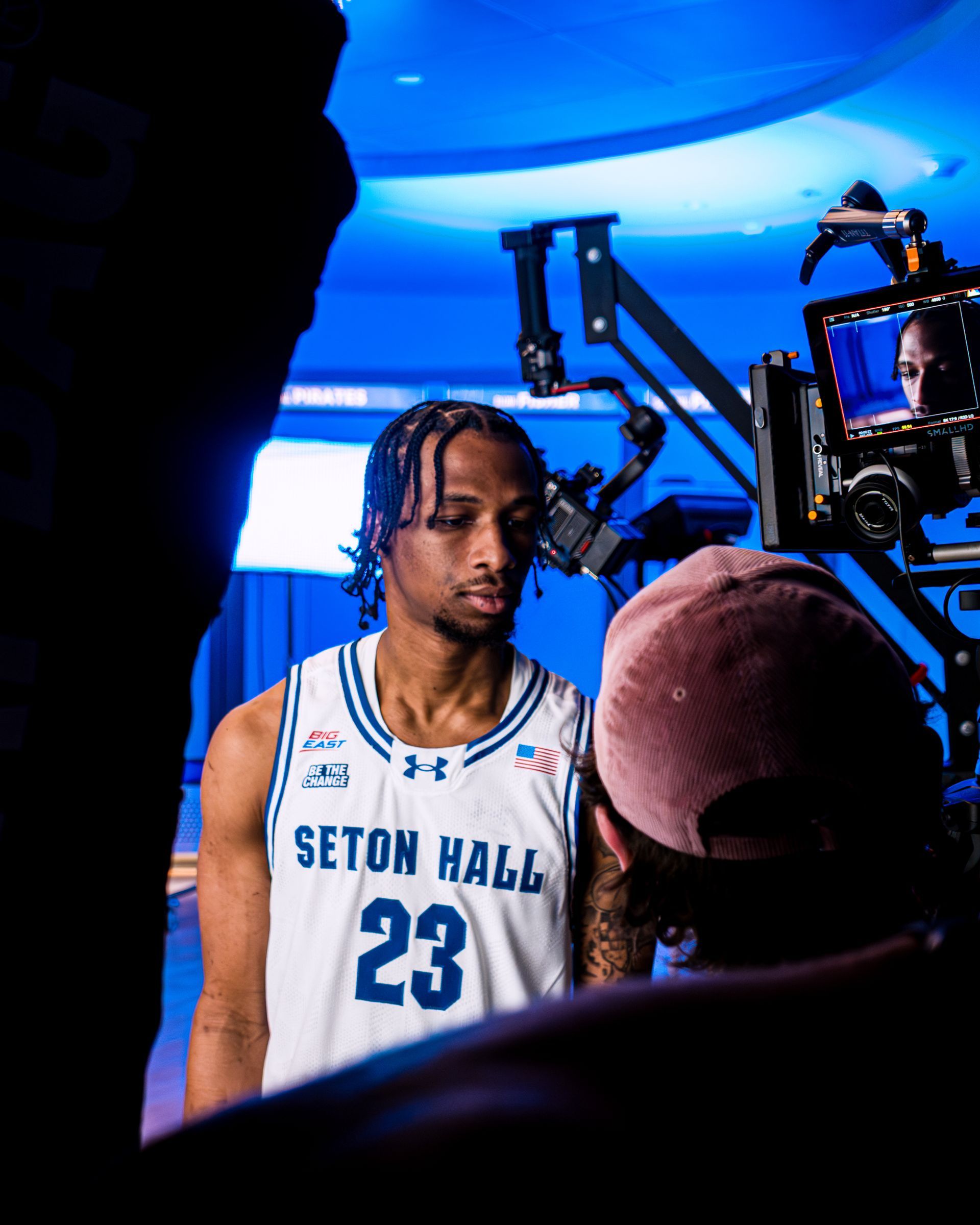 Seton Hall basketball player in white jersey stands under blue lighting during a media shoot
