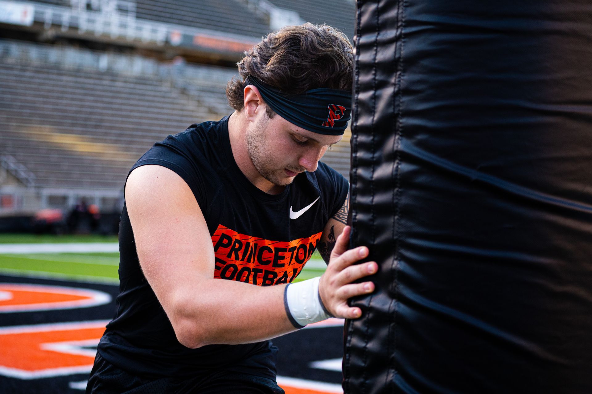 Football player in black and orange pushing against a padded tackling dummy on a field