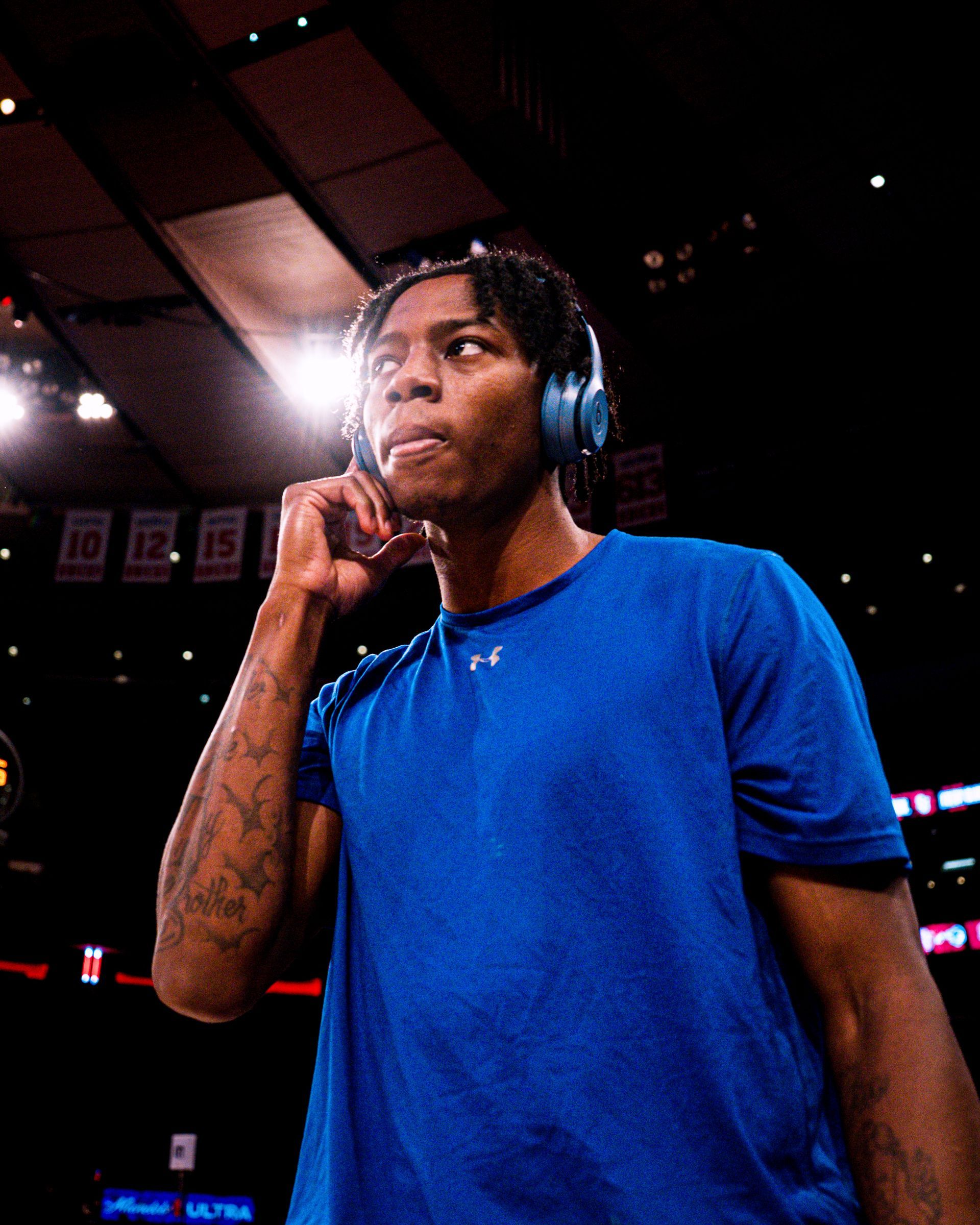Basketball player in a blue shirt wearing headphones, standing on the court with a thoughtful expression.