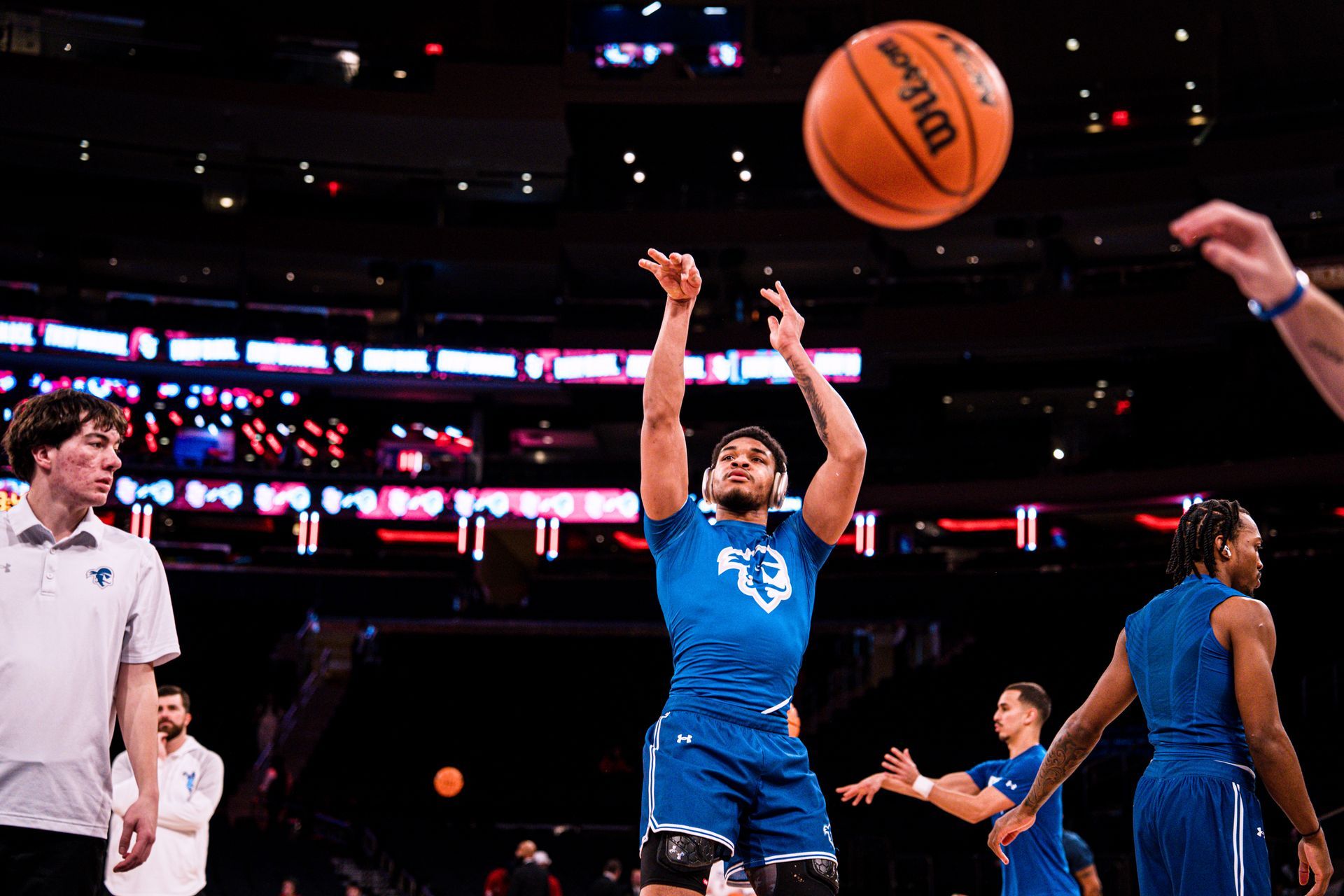 Basketball player in blue shoots during a game, with a referee and other players nearby.