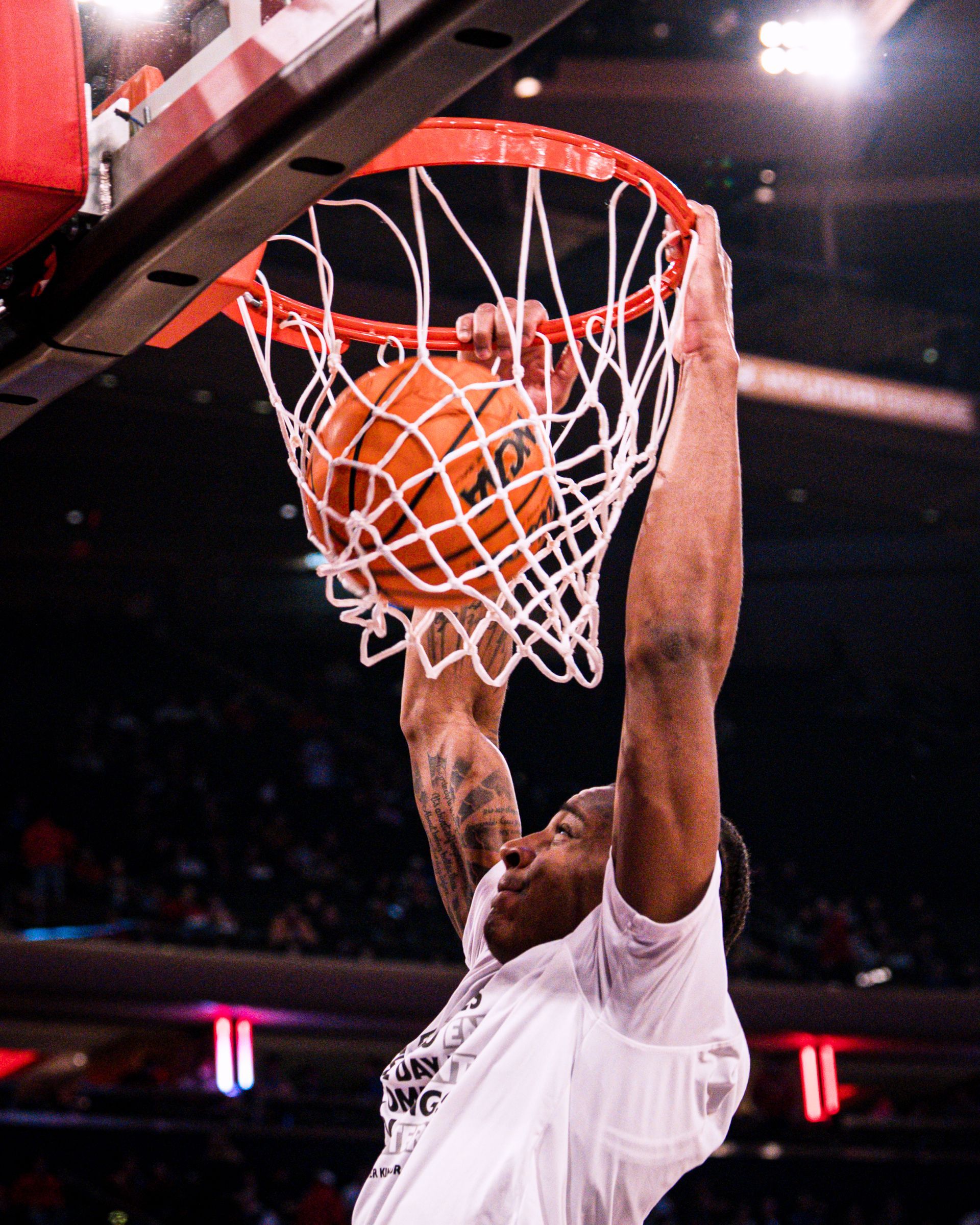 Basketball player dunking orange ball through red rim and white net on a dark court