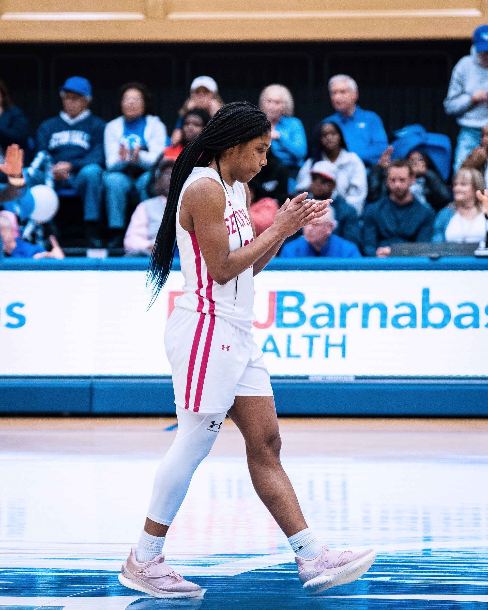 Basketball player in white and red uniform walking on court with crowd in the background