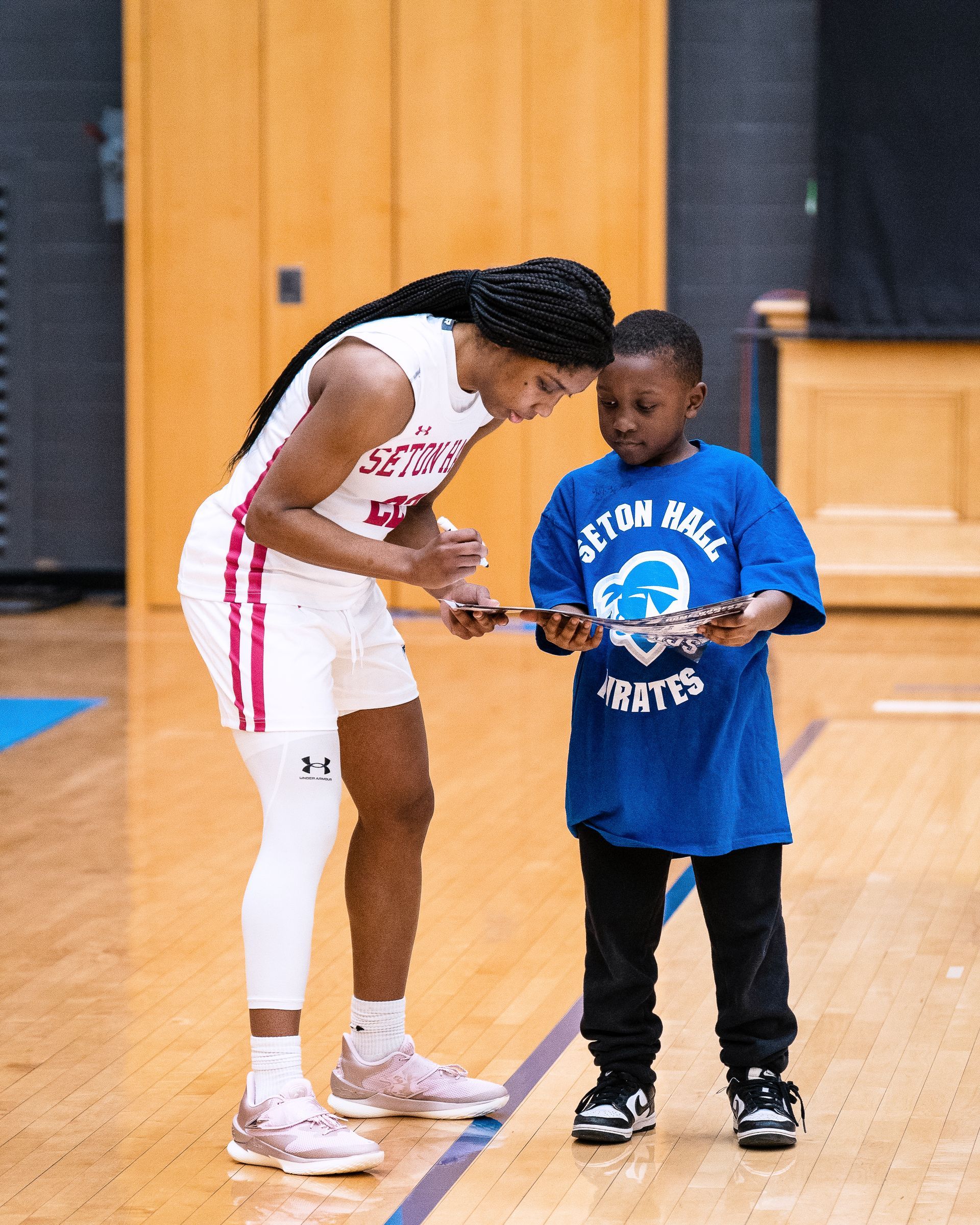 Adult in white athletic uniform points at a child in a blue shirt on an indoor gym floor.