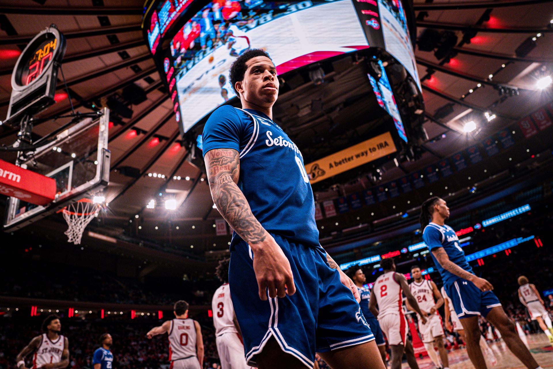 Basketball player in blue uniform stands on court under bright arena lights during a game