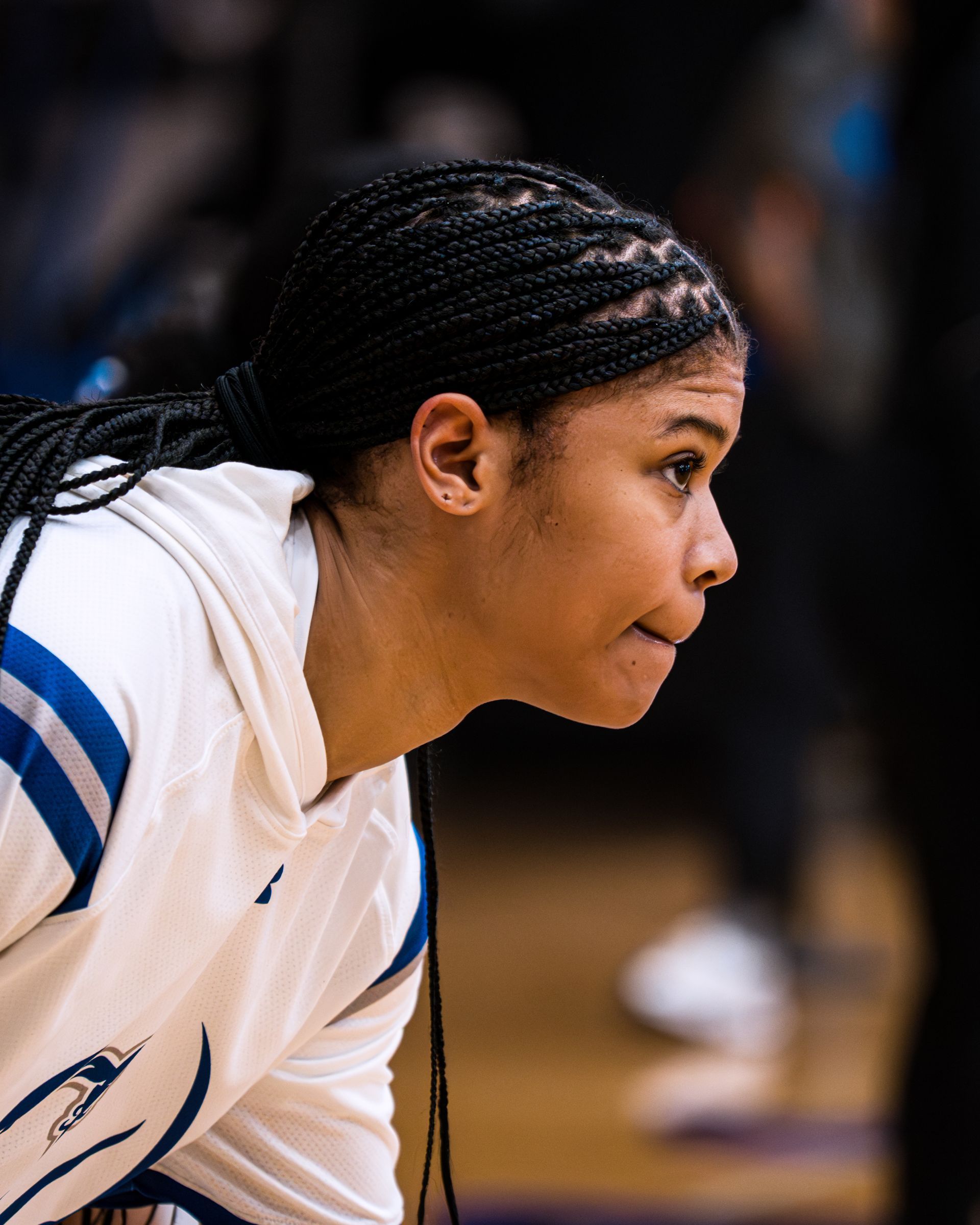 Basketball player in white jersey crouches in focus on the court, looking ahead with concentration.