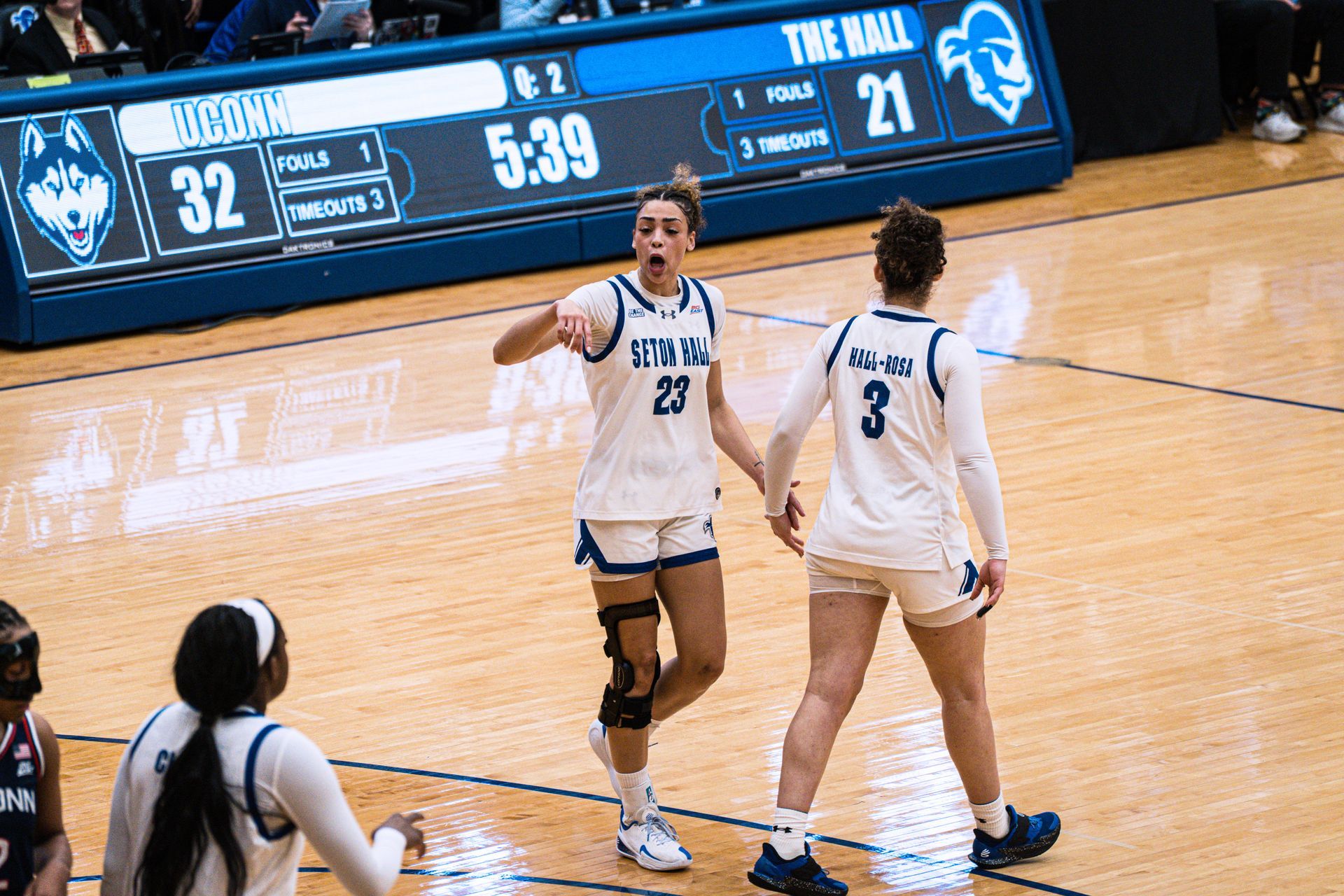 Two basketball players in white uniforms celebrate on court during a game.