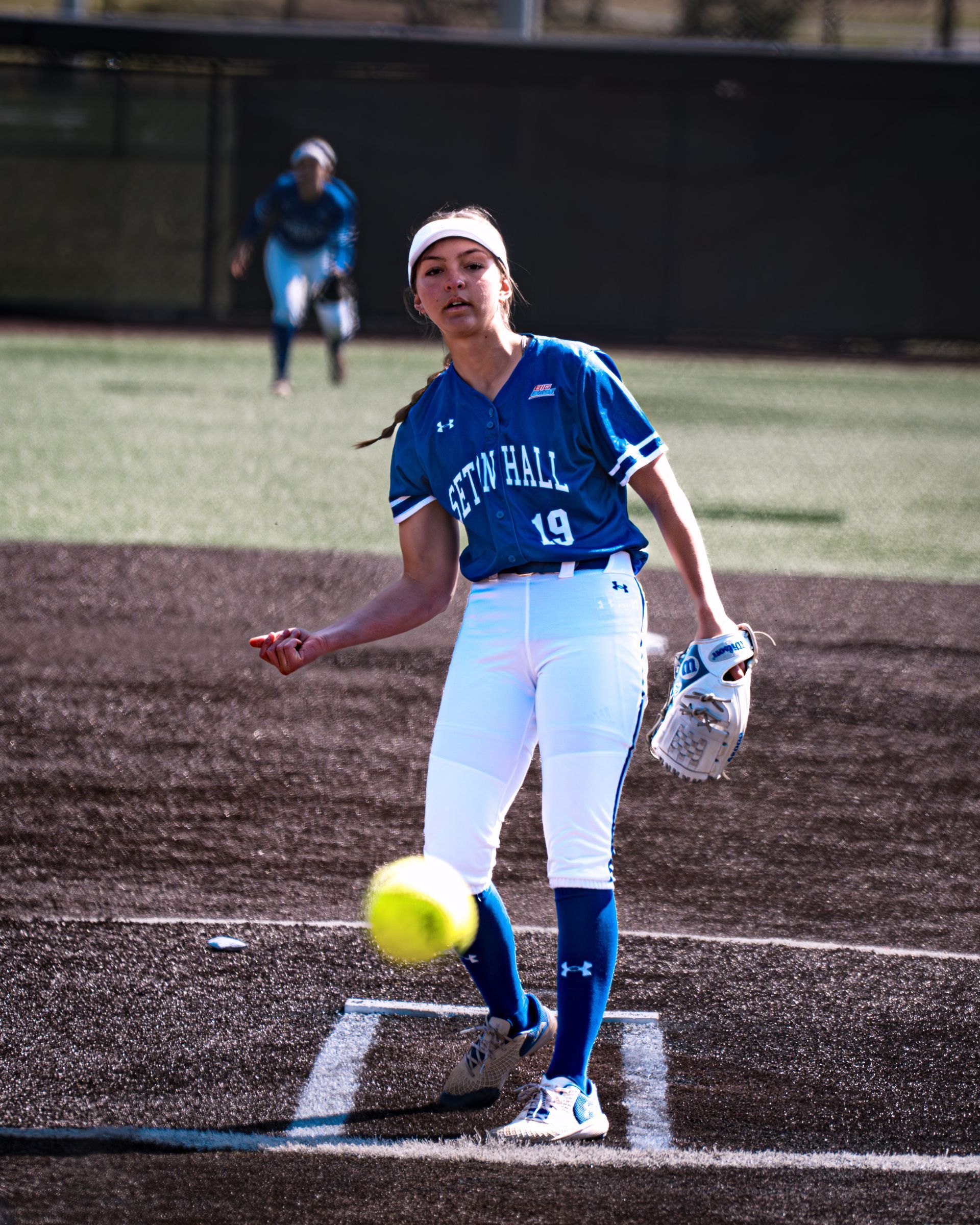 Softball pitcher in blue uniform winding up to throw on the field