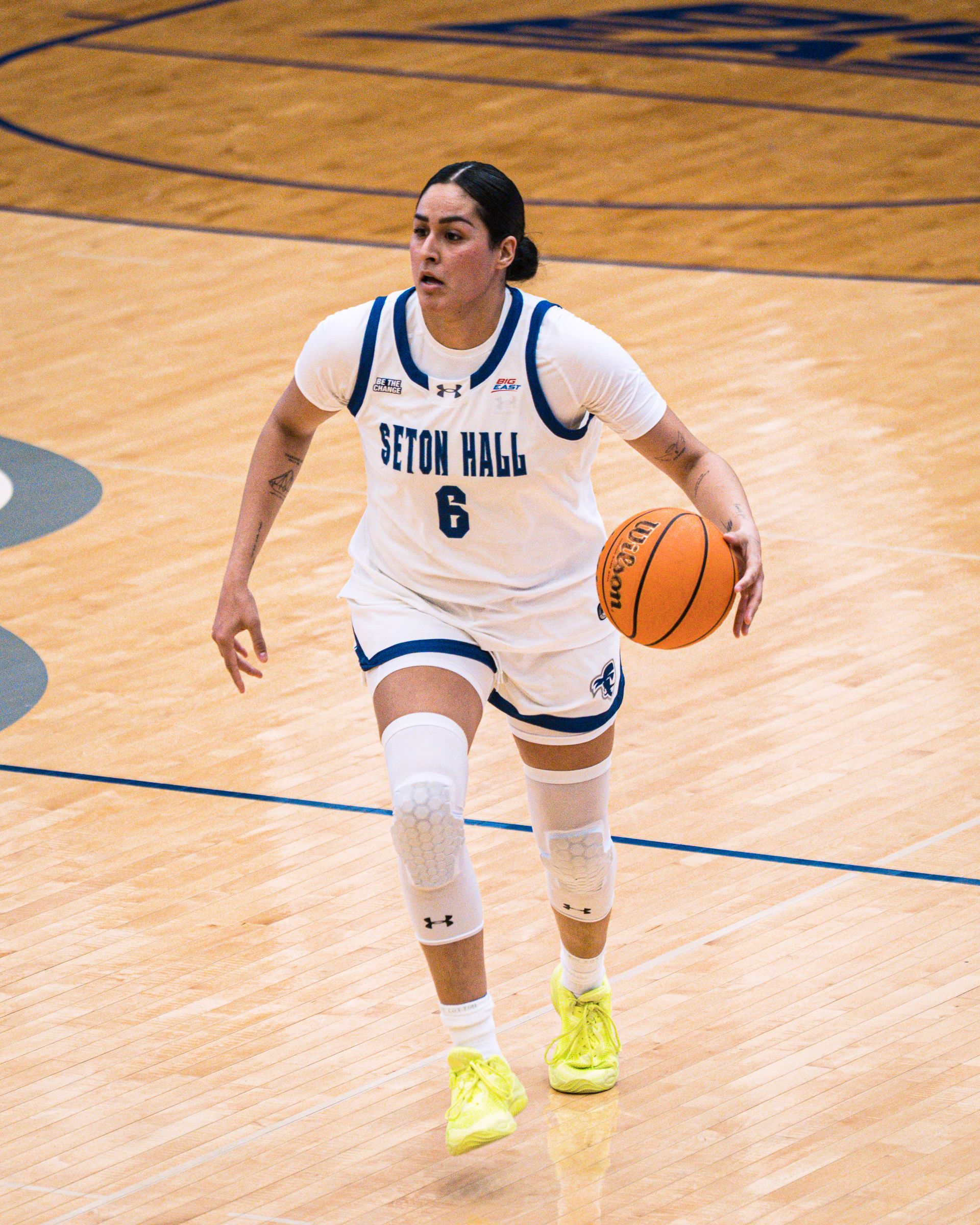 Seton Hall basketball player dribbles on court in white uniform and neon shoes