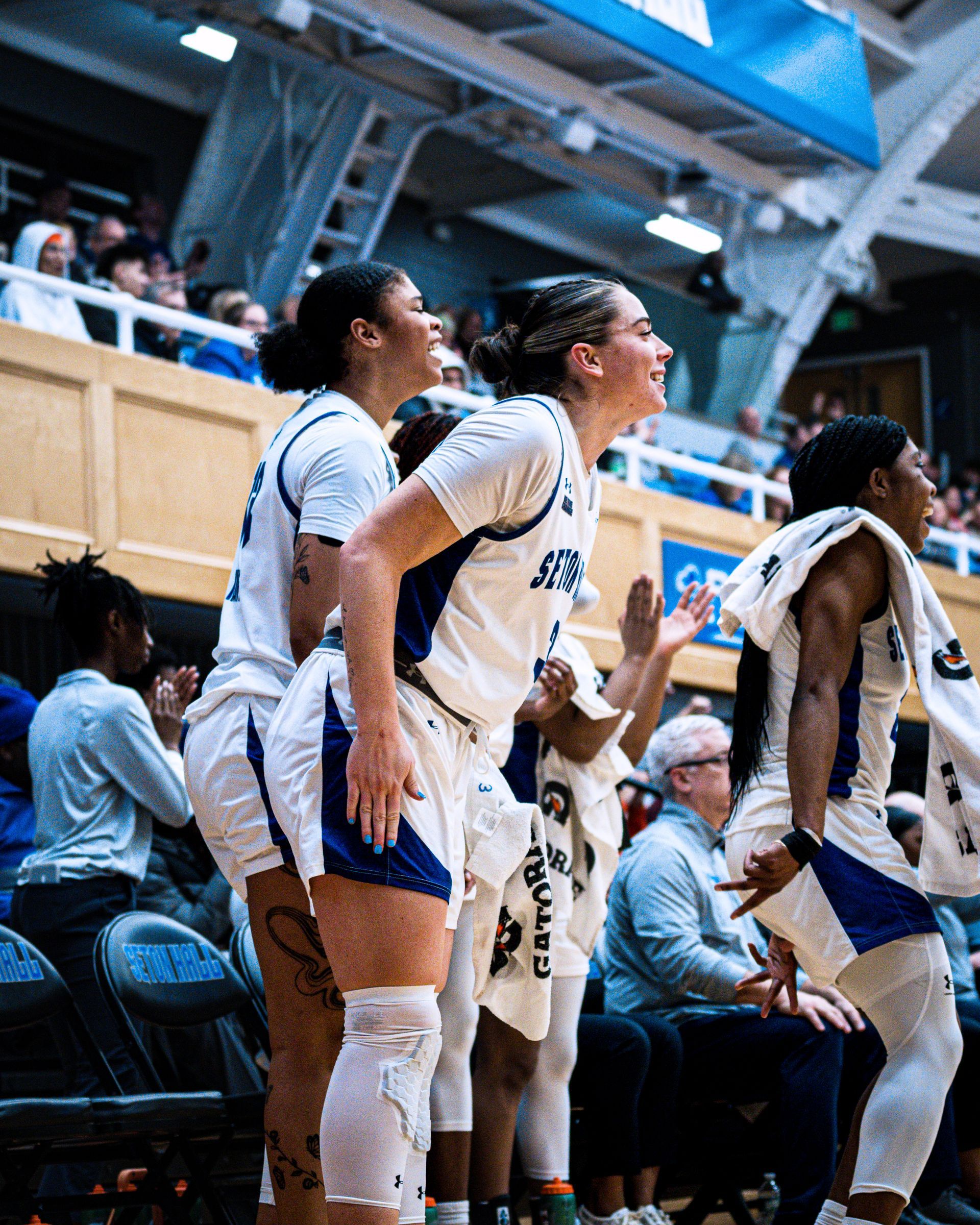 Basketball players in white uniforms standing and cheering on the sideline during a game