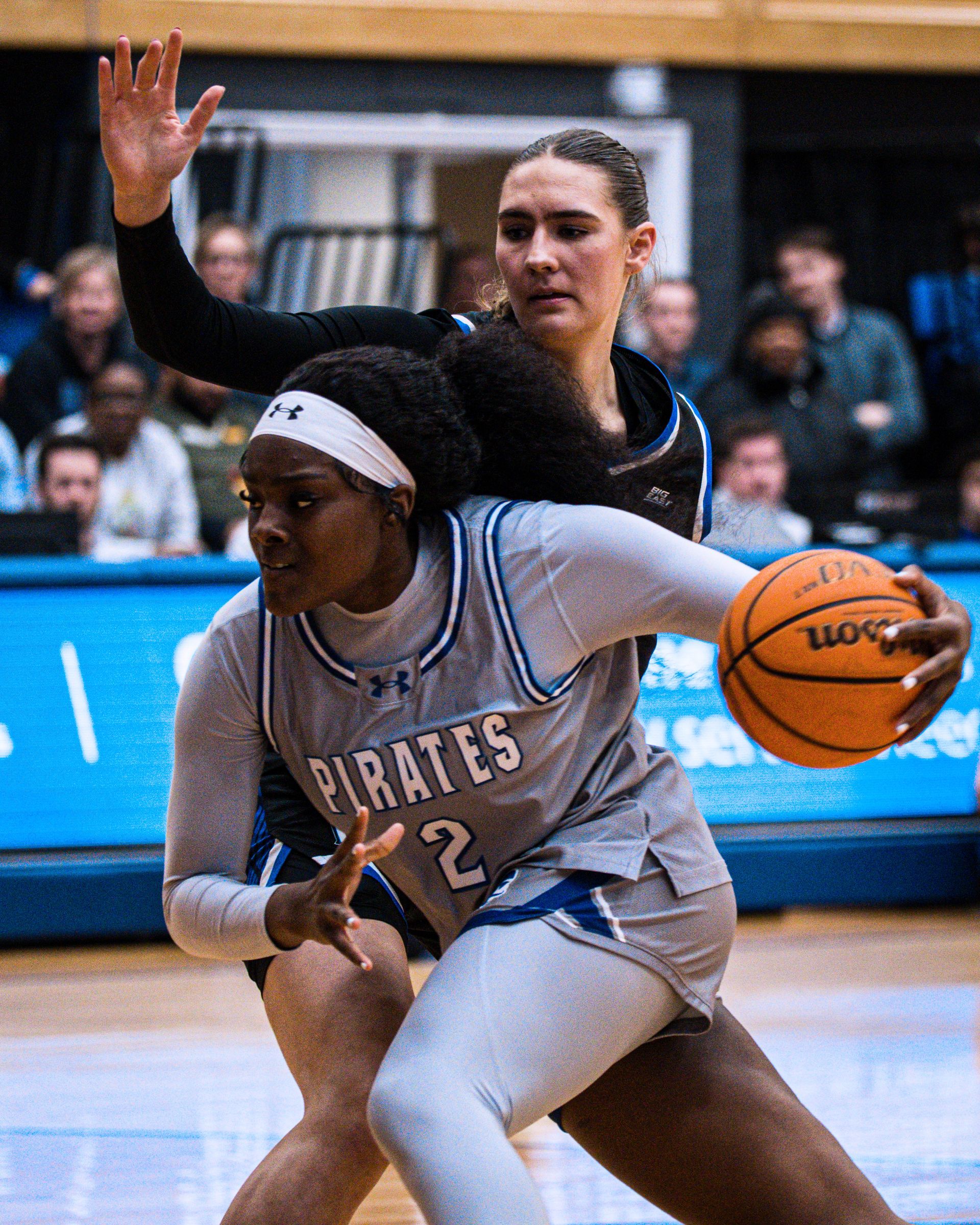 Basketball player in gray dribbles while shielding the ball from a defender in black