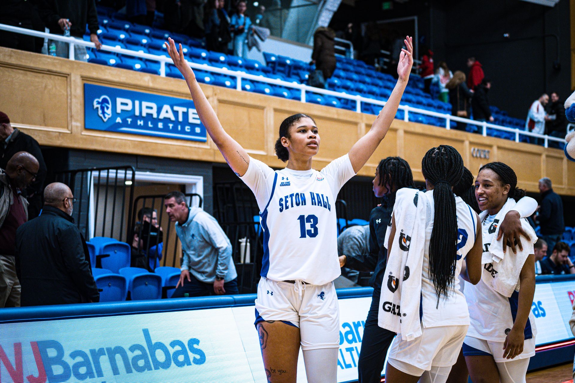 Basketball player in white jersey raises both arms while teammates celebrate on the court.