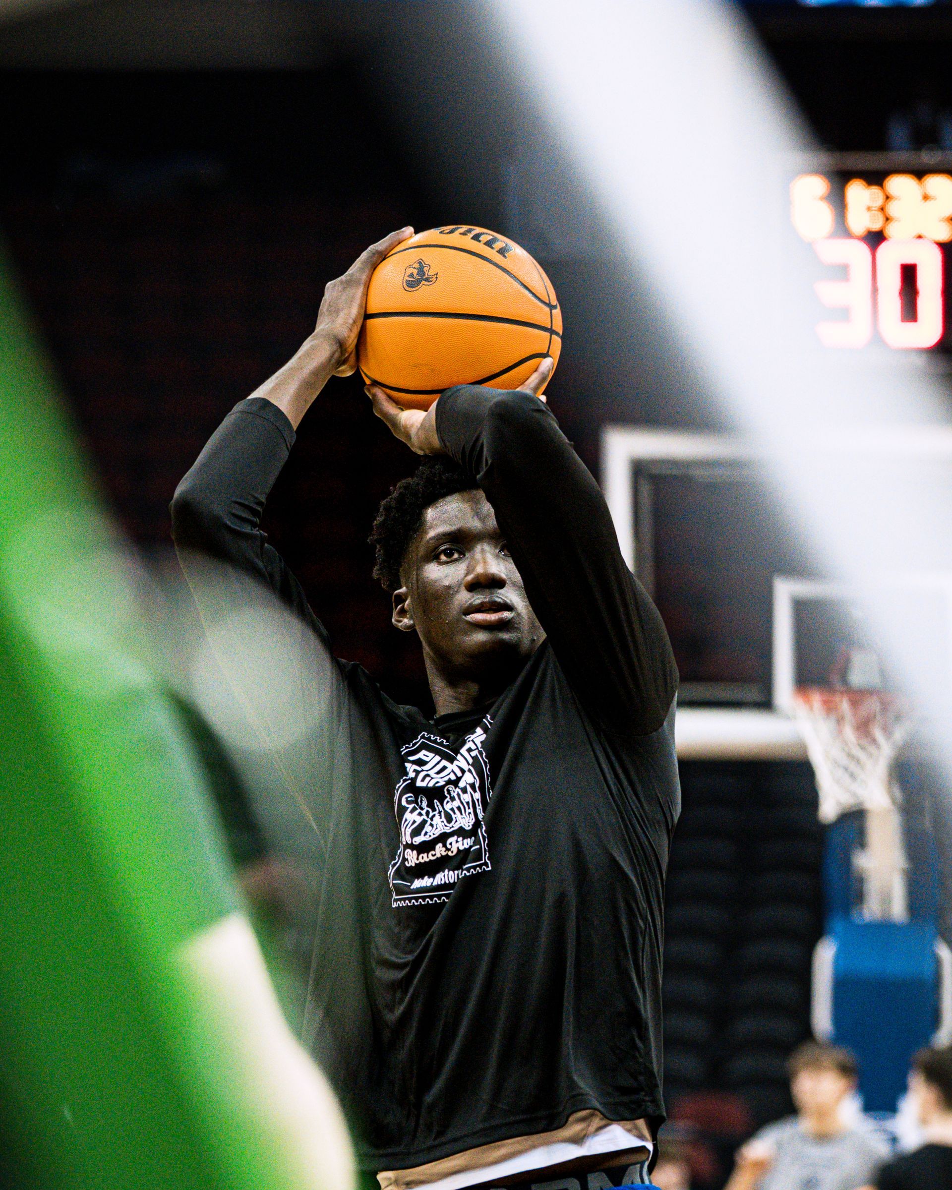 Basketball player in black shirt holding a ball overhead on an indoor court