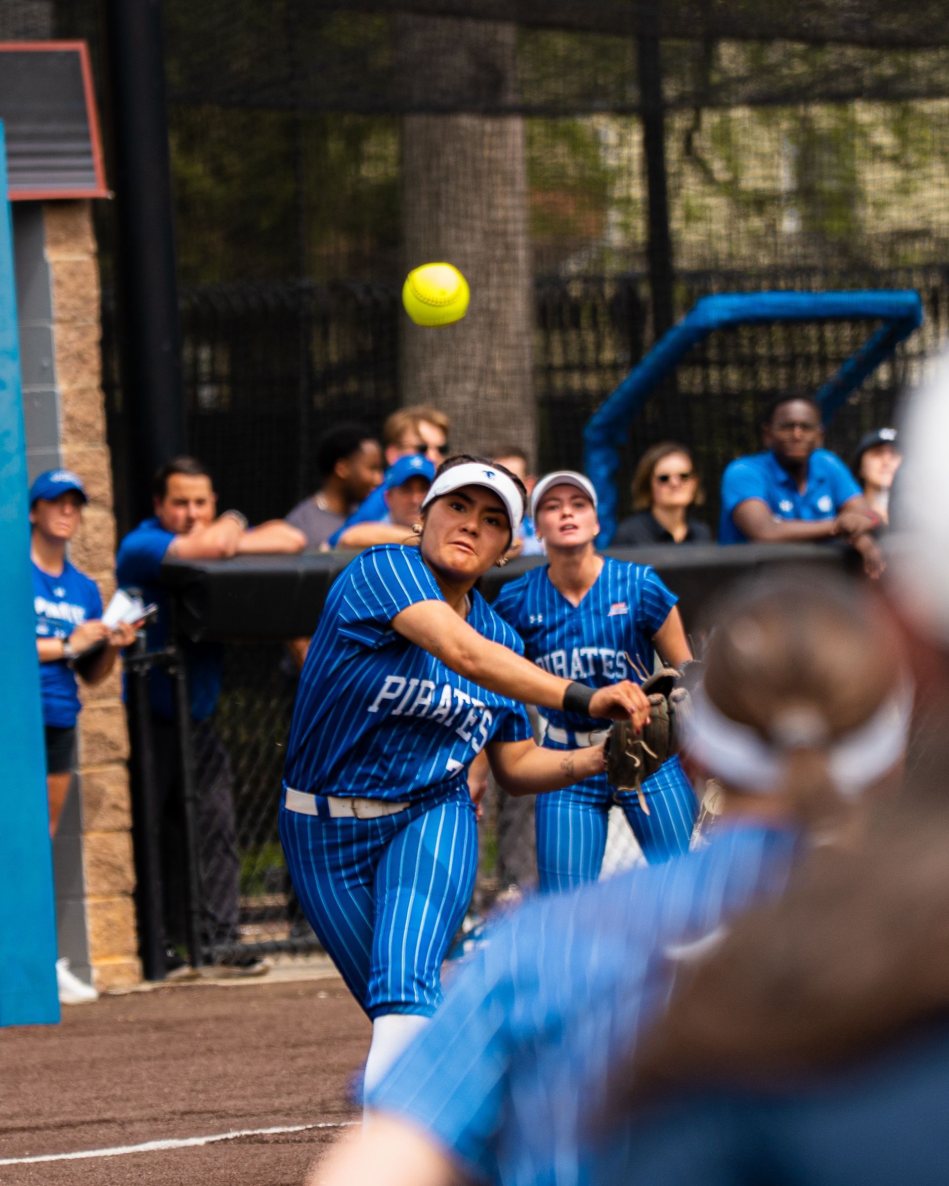 Blue-uniformed softball players field a high fly ball near the dugout.