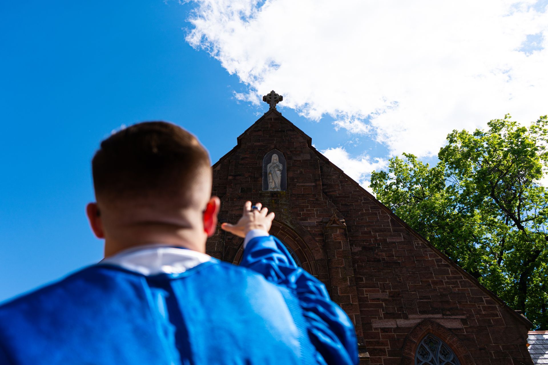Person in blue jacket pointing at a brick building under a bright blue sky
