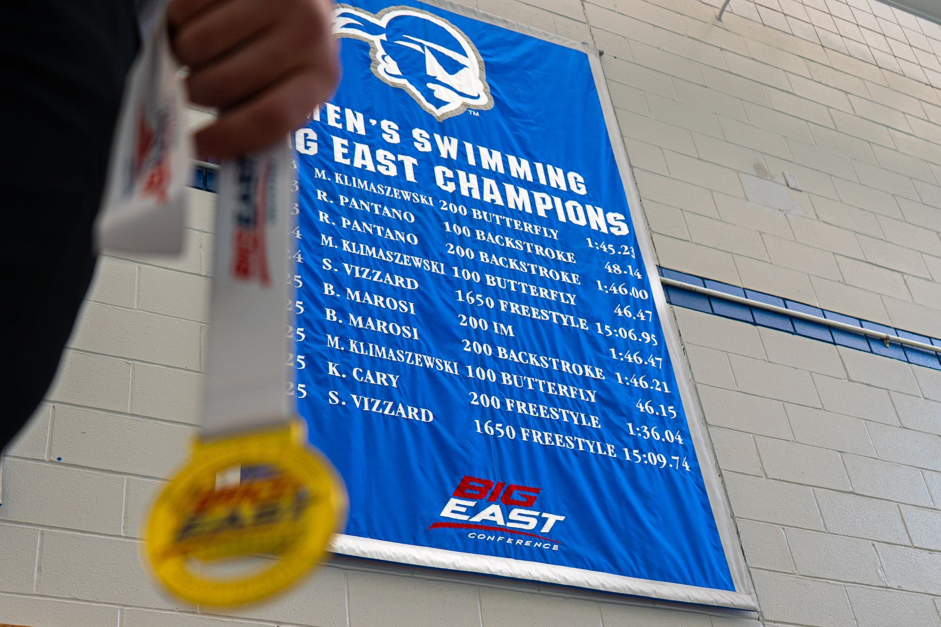 Child holding a gold medal in front of a blue East swimming championships banner.