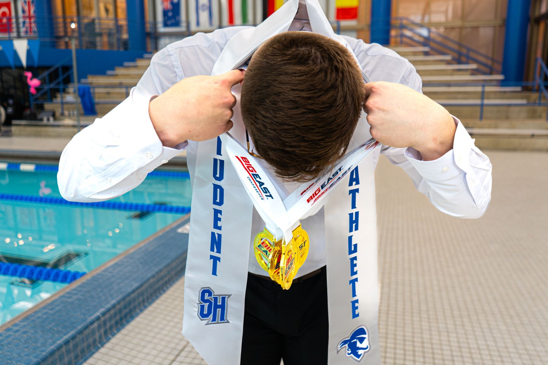 Swimmer at poolside looking down at medal and ribbon around neck